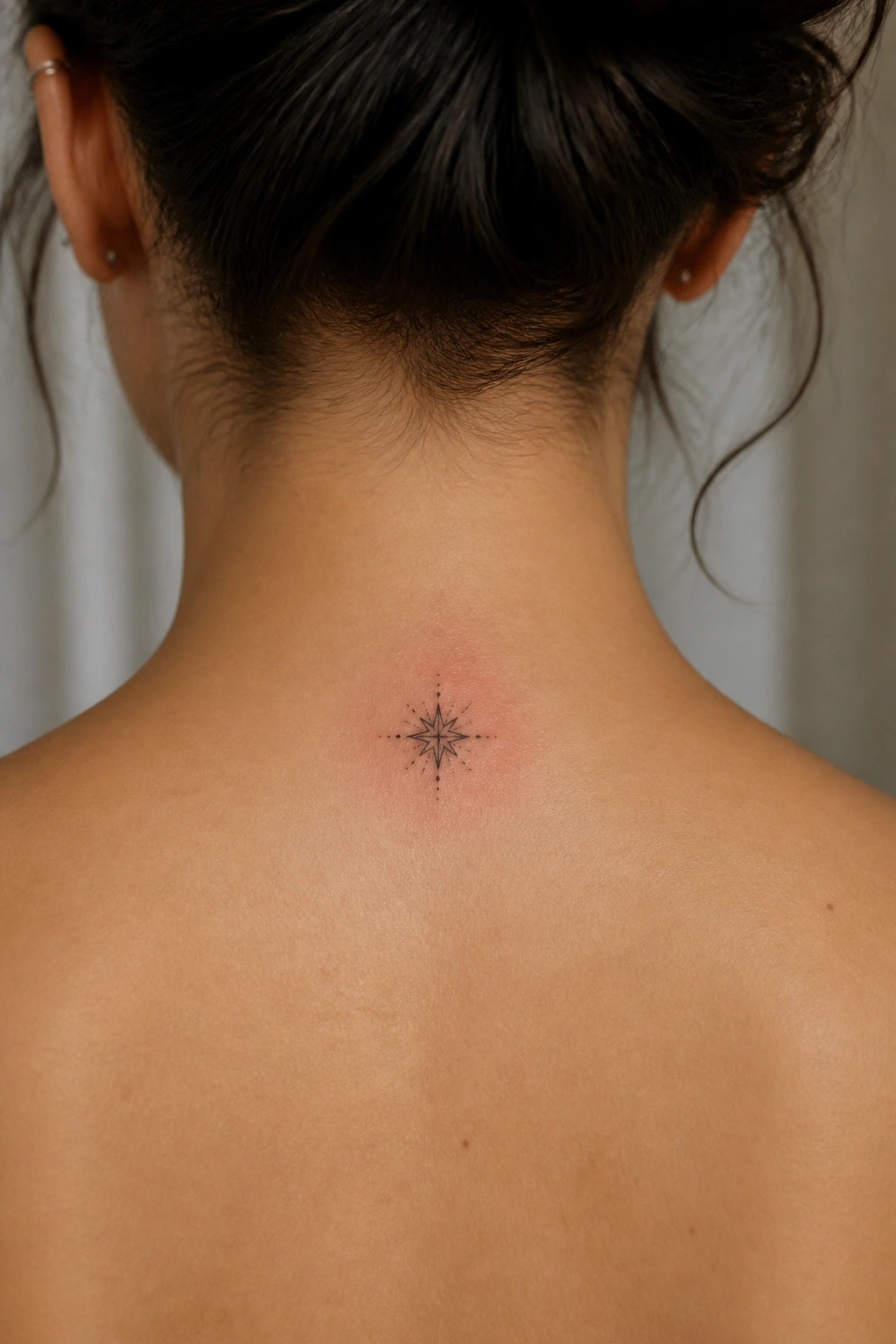 Woman with dark hair in bun shows star tattoo on reddened neck skin