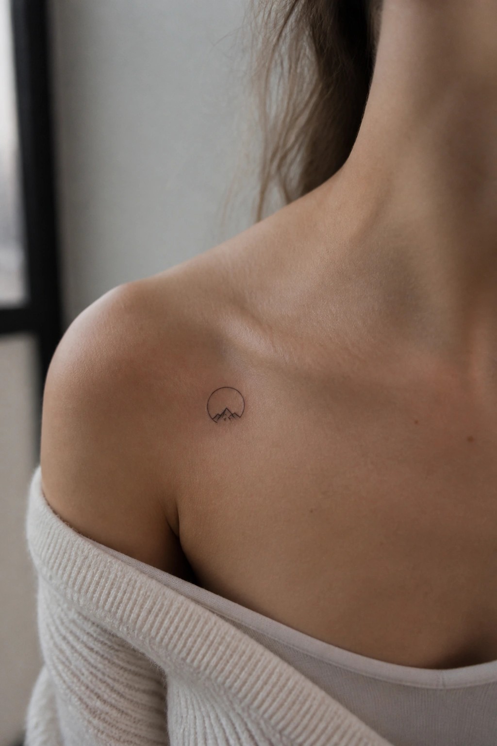 Minimalist line art tattoo of mountains inside a circle on a woman's shoulder