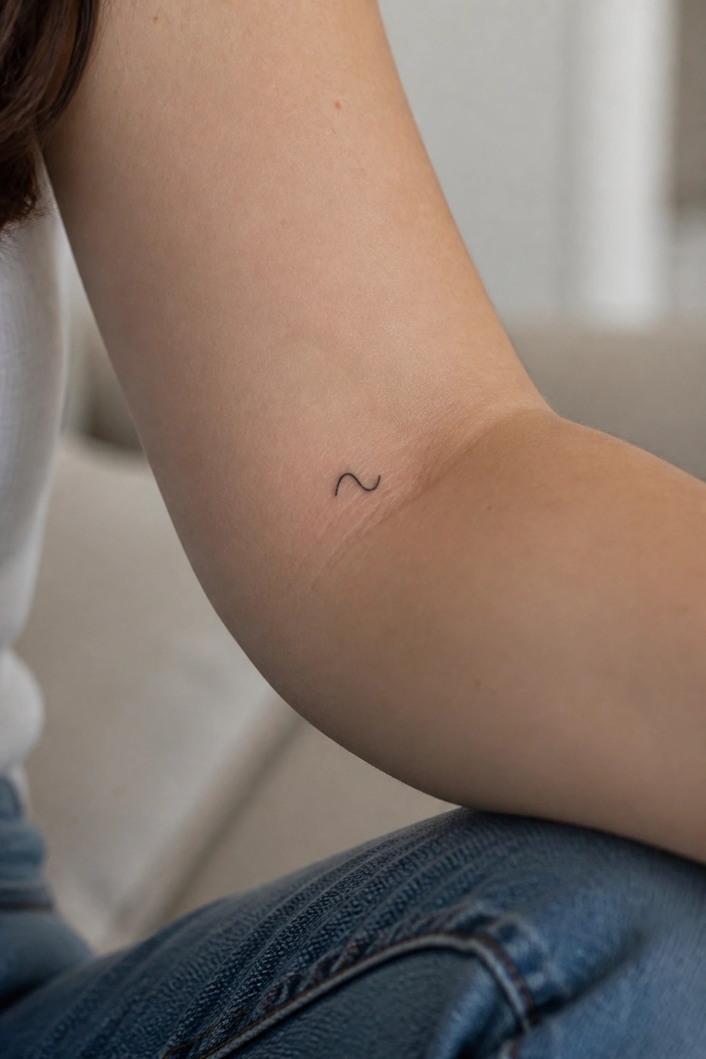 Arm with small black wavy tattoo, wearing white shirt and blue jeans