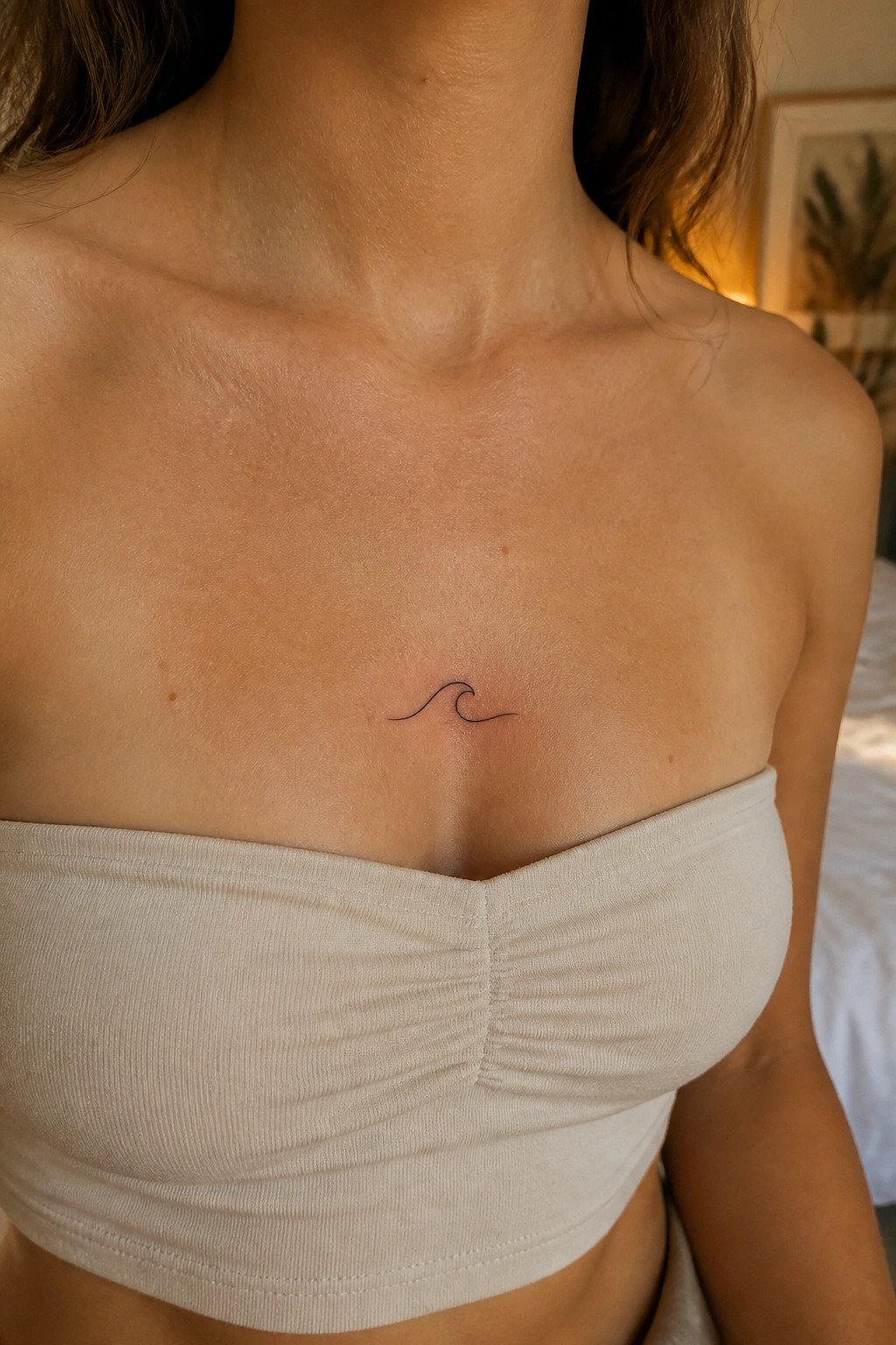 Small wave tattoo centered on chest above beige strapless top