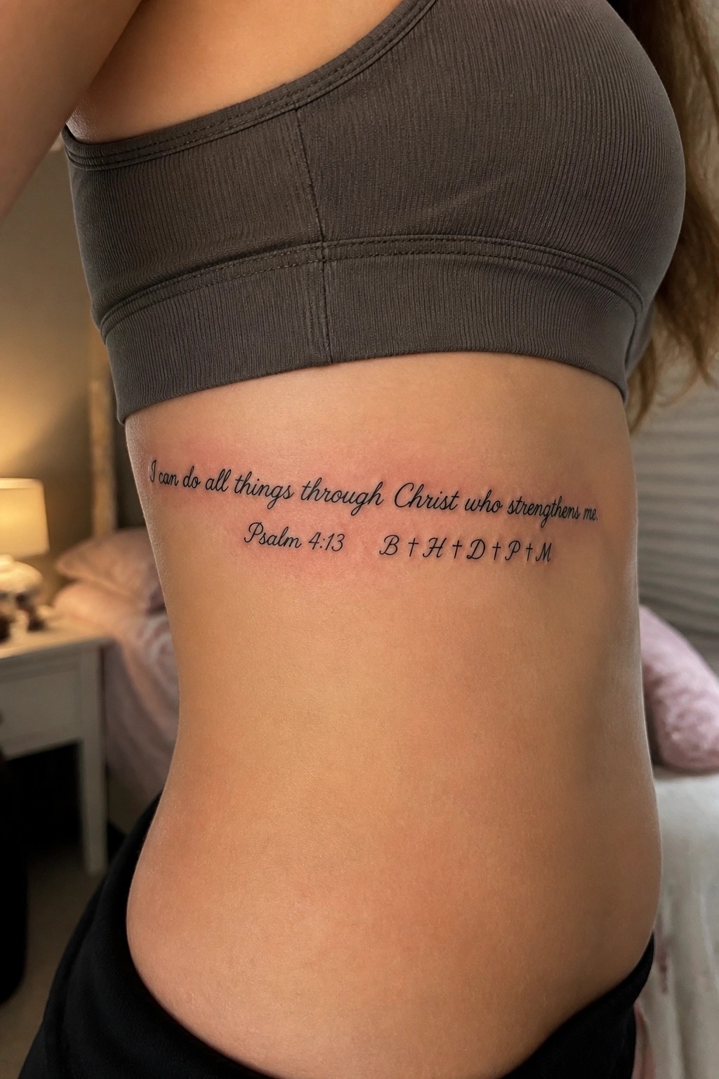Black script tattoo of a bible verse on the side torso with psalm reference and five family initials in a delicate font.