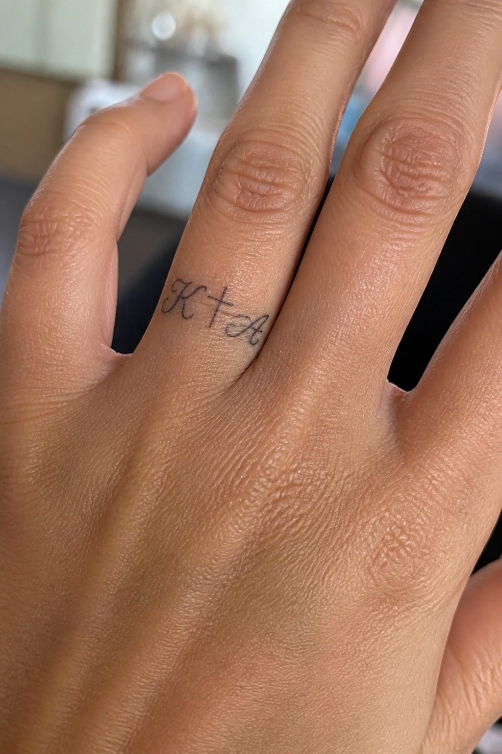 Small script tattoo on the side of a finger showing the initials K and A with a cross between them.