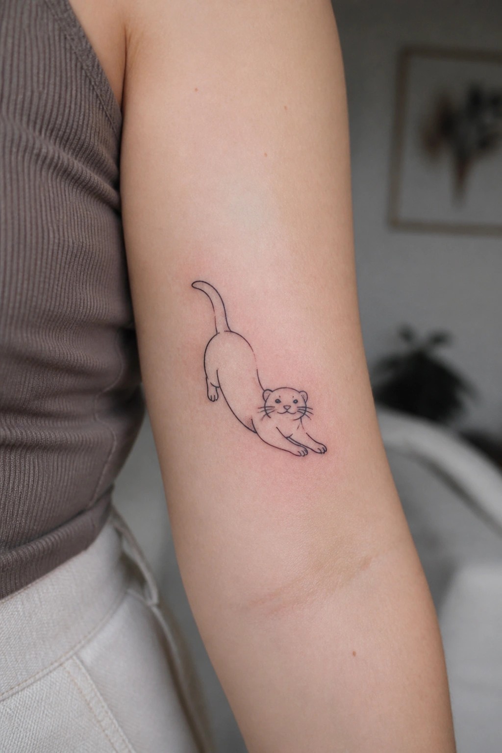 Minimalist black line tattoo of an otter stretched across the upper arm in a simple outline style