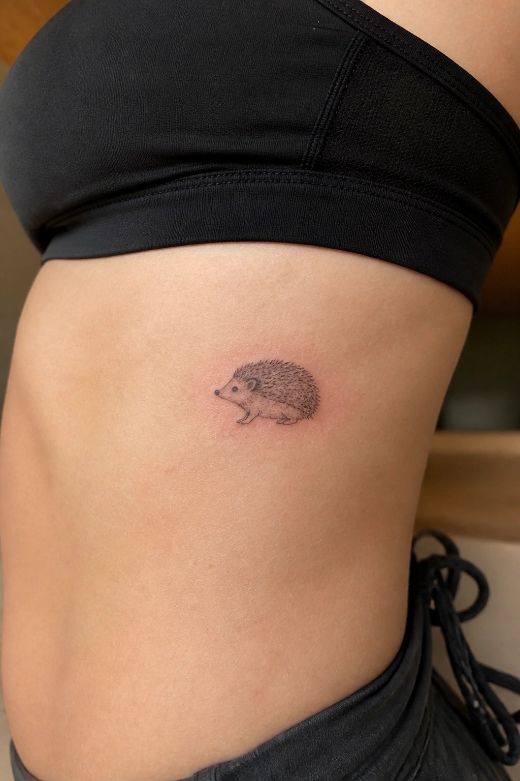 Small hedgehog tattoo on skin below black sports bra top