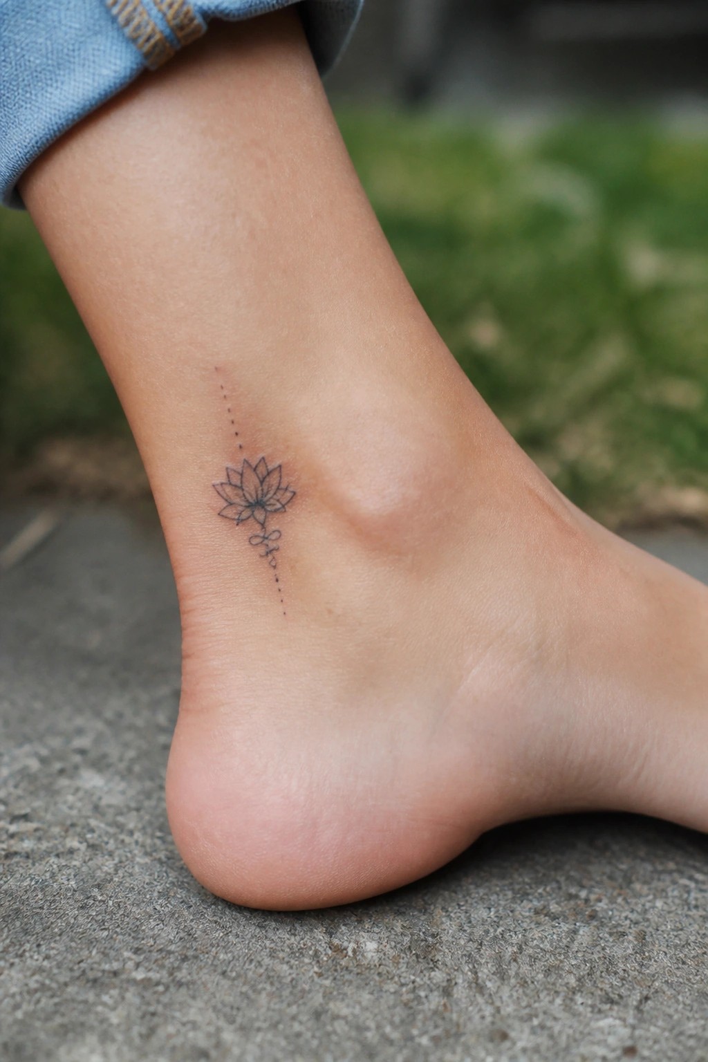 Small lotus flower tattoo on the ankle with dotted vertical line and infinity symbol below