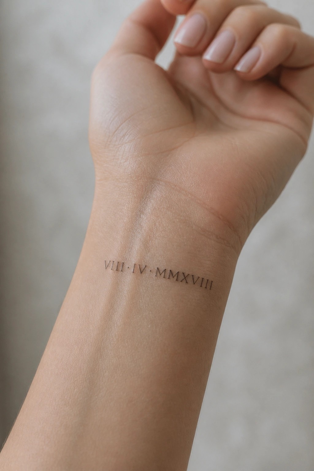 Close-up of a small fine-line Roman numeral date tattoo on the inner wrist reading VIII IV MMXVIII
