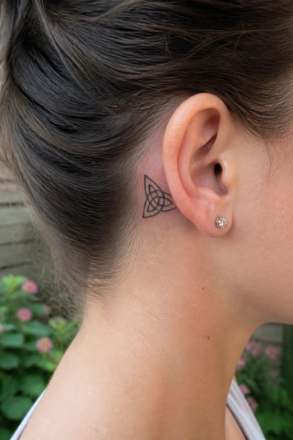 Close-up of neck with Celtic knot tattoo behind ear and diamond stud earring.