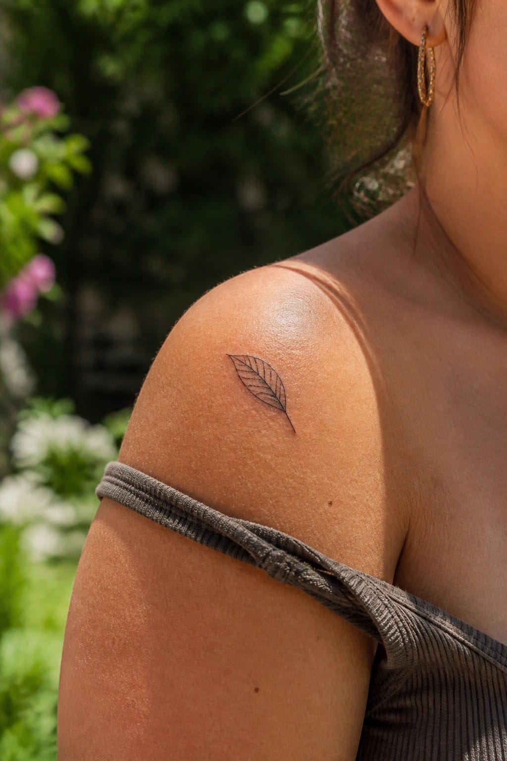 Small leaf tattoo on tanned shoulder with gray off-shoulder top in sunlight