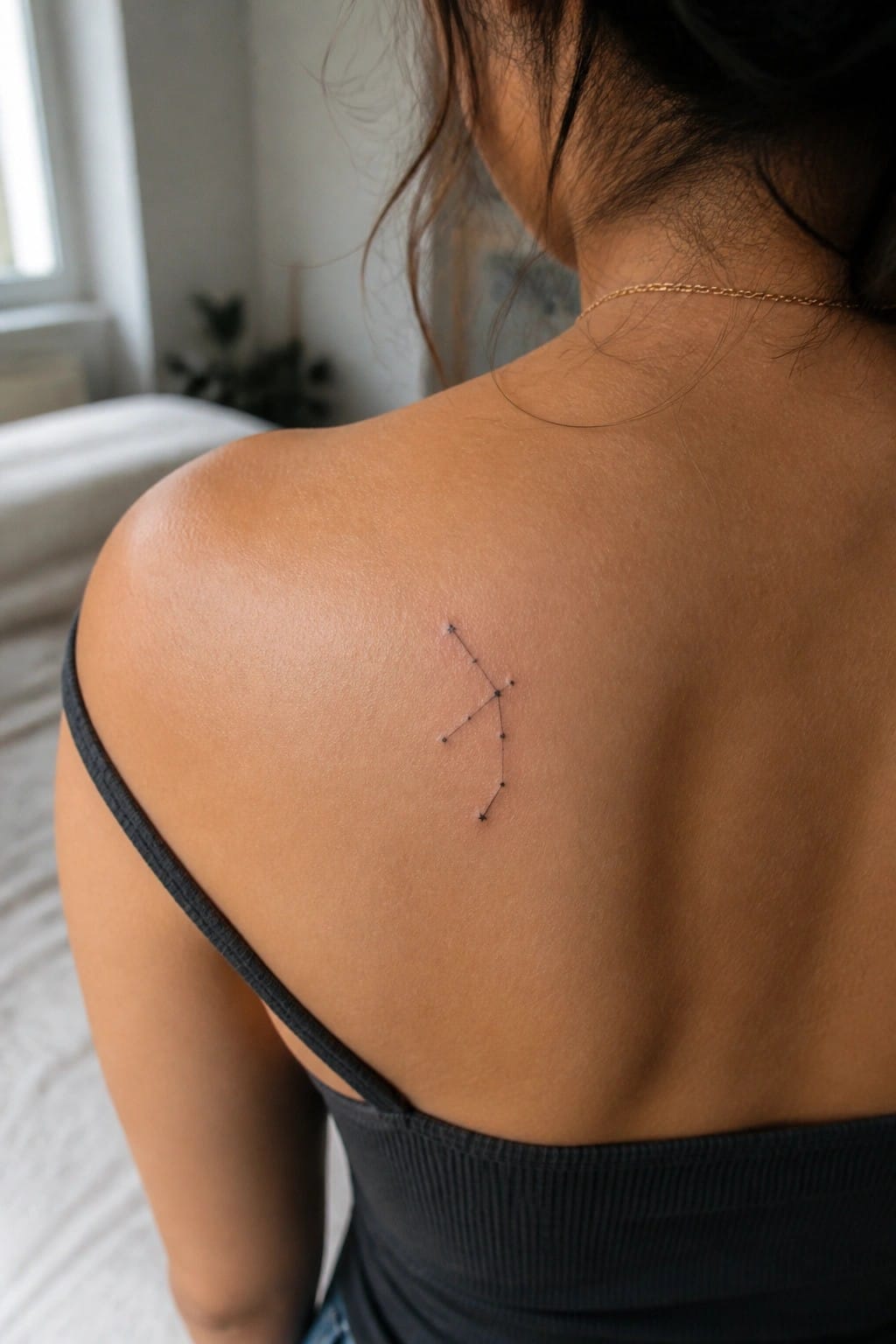 Woman's upper back with constellation tattoo above black off-shoulder top and gold necklace