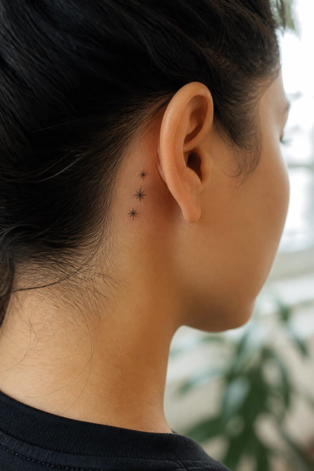 Three small black star tattoos behind ear on person's neck with dark hair