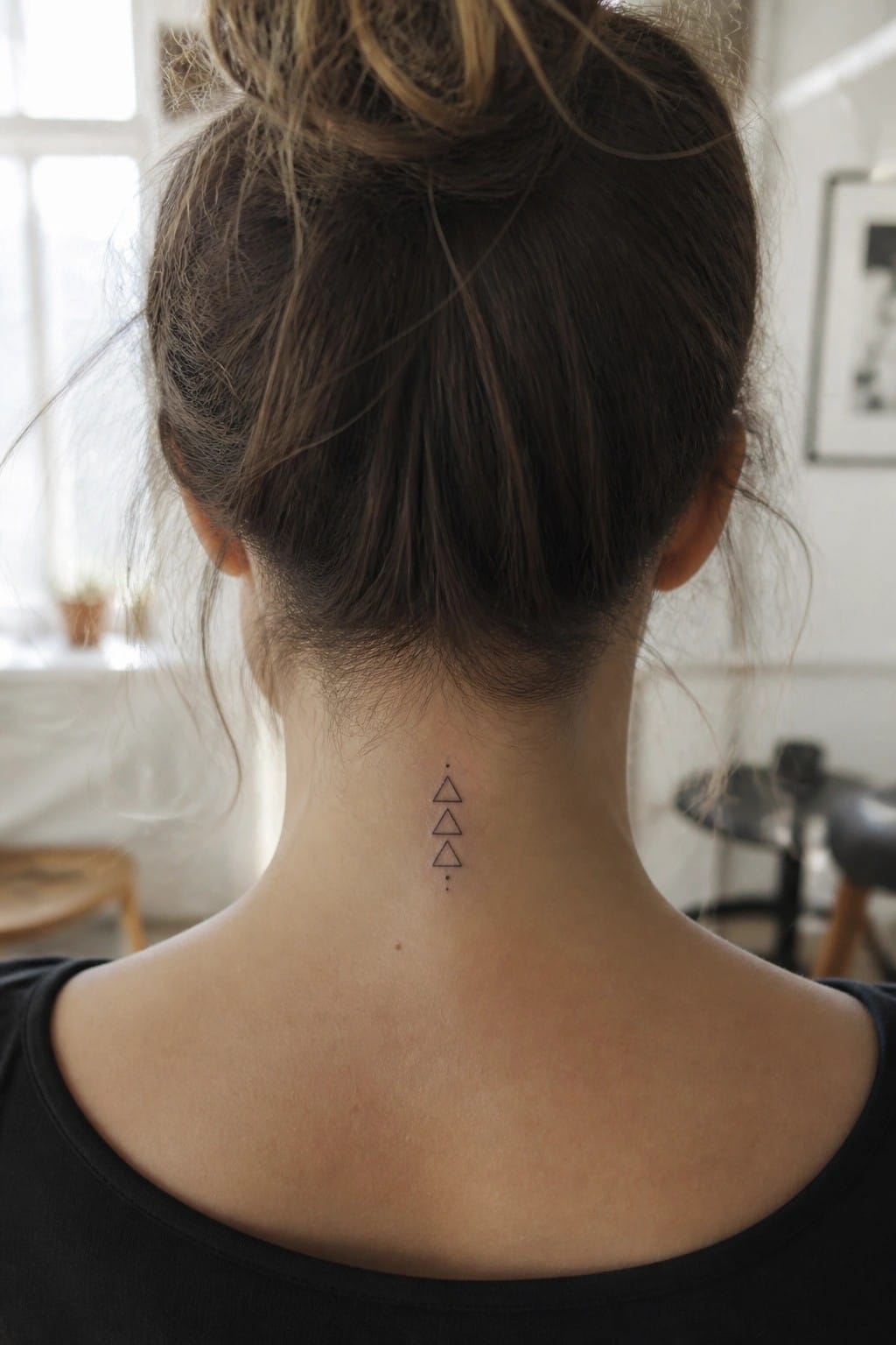 Minimalist line tattoo of three stacked triangles with dots above and below on the back of a woman's neck
