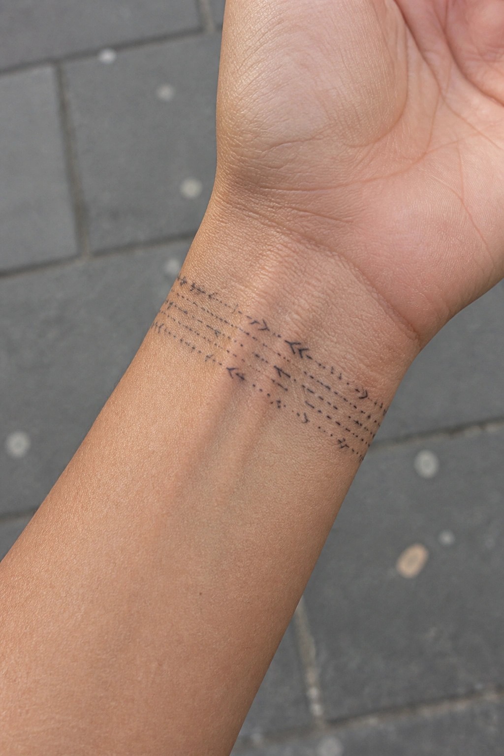 Wrist tattoo with multiple rows of dashed lines and arrows on skin.
