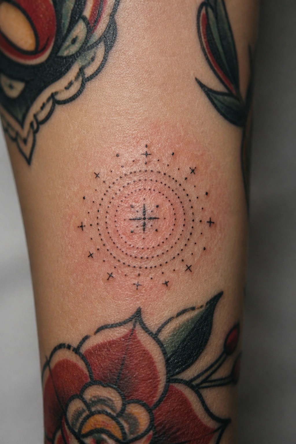 Fresh black dotwork circle tattoo with crosses above colorful floral designs on skin