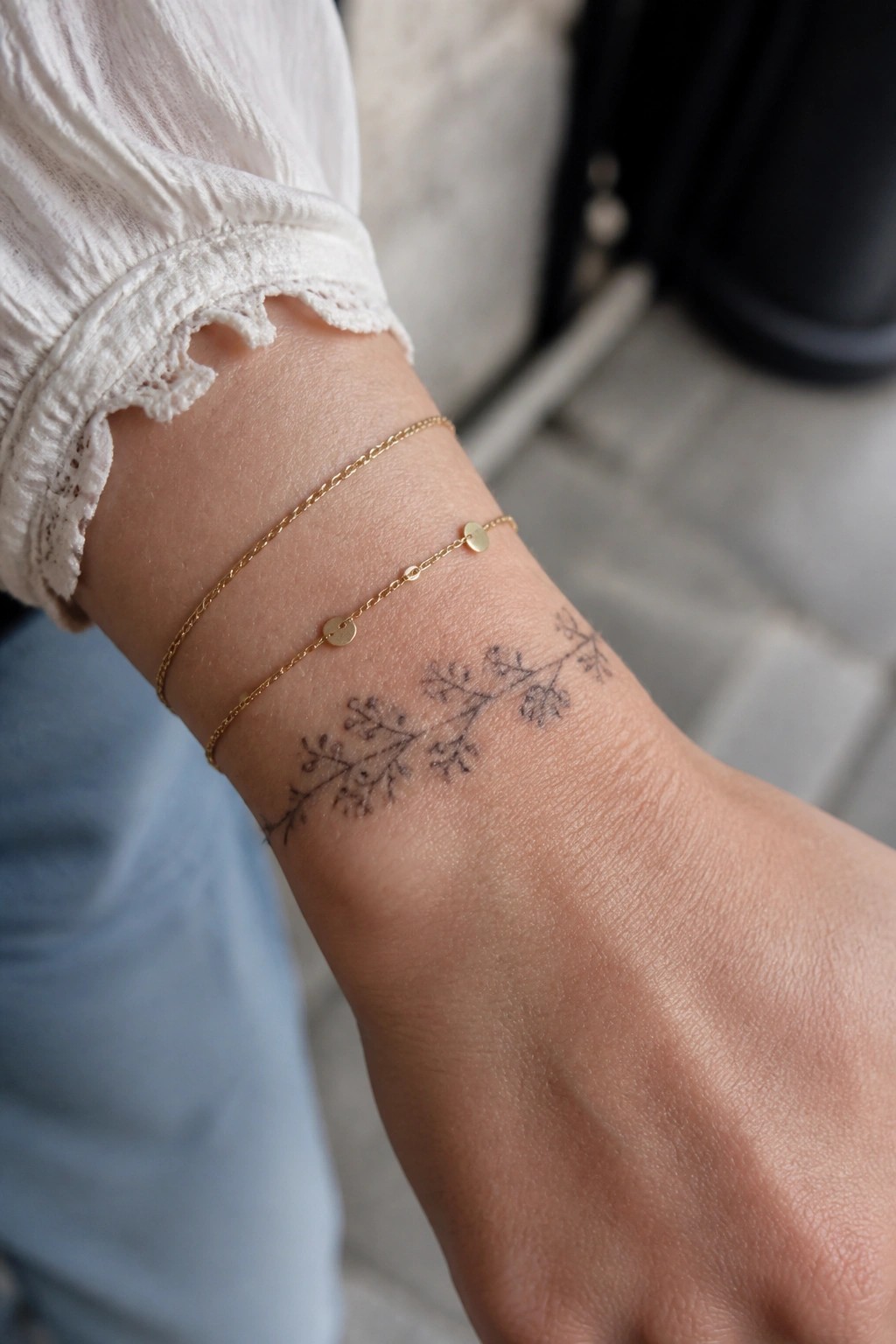 Gold bracelets and floral tattoo on wrist with white ruffled sleeve