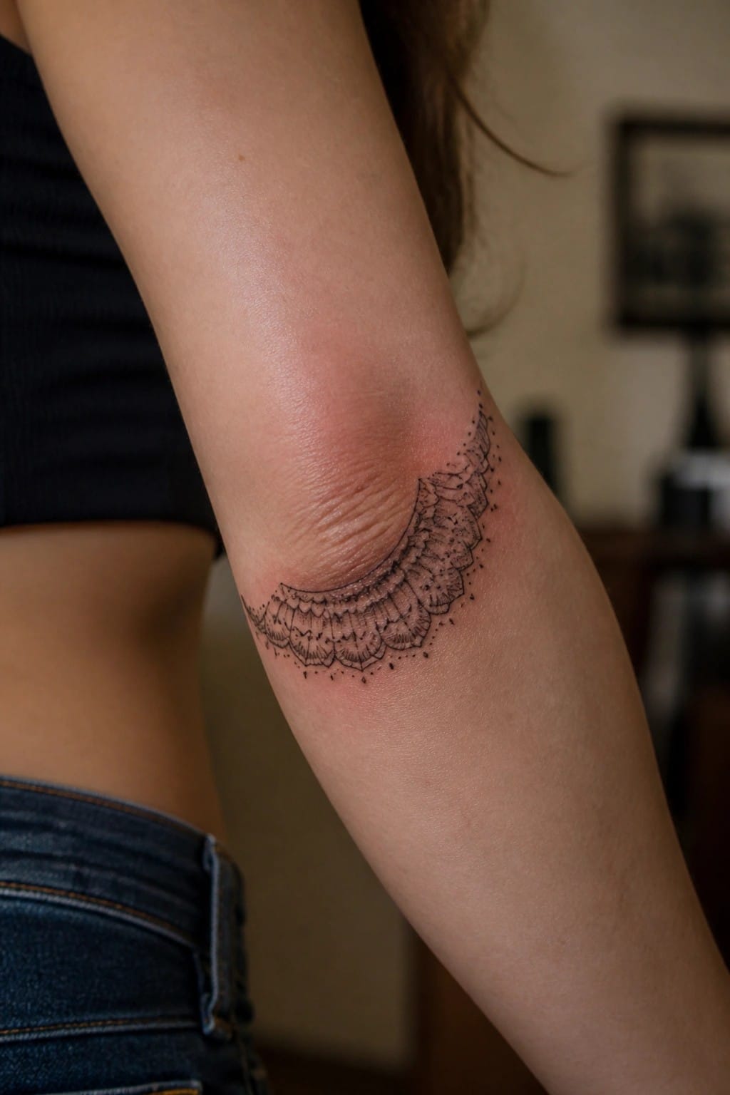 Black fine line tattoo of a curved scalloped pattern placed along the inner elbow crease
