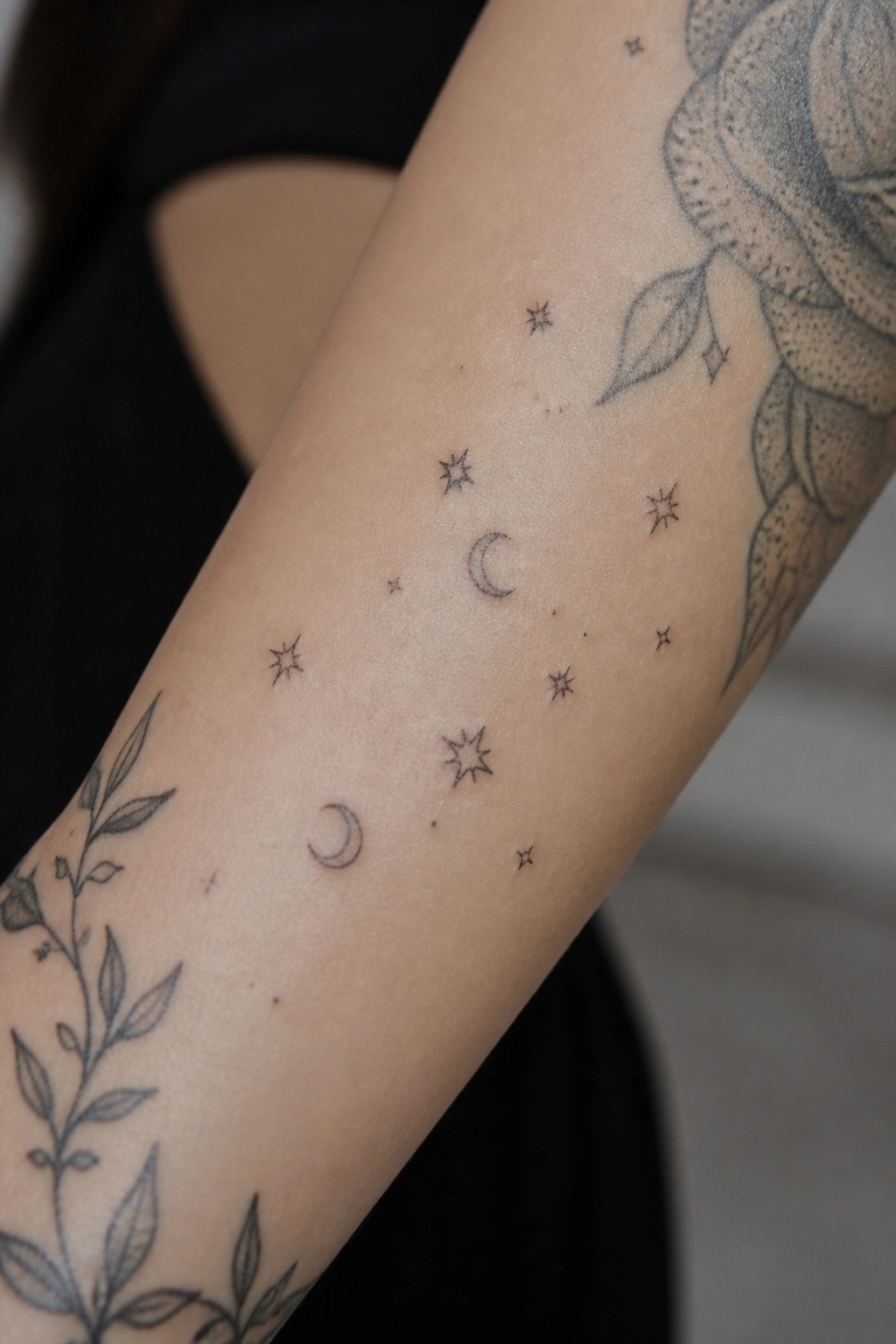 Fine line stars and crescent moons placed on the inner forearm as filler tattoos around floral designs