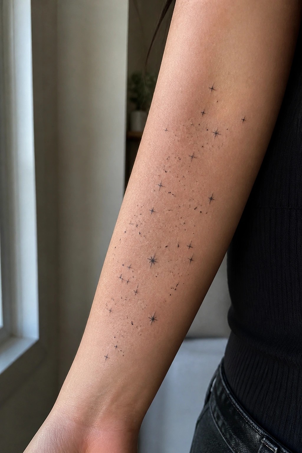 Arm with scattered black star tattoos, black sleeveless top, light indoor background.