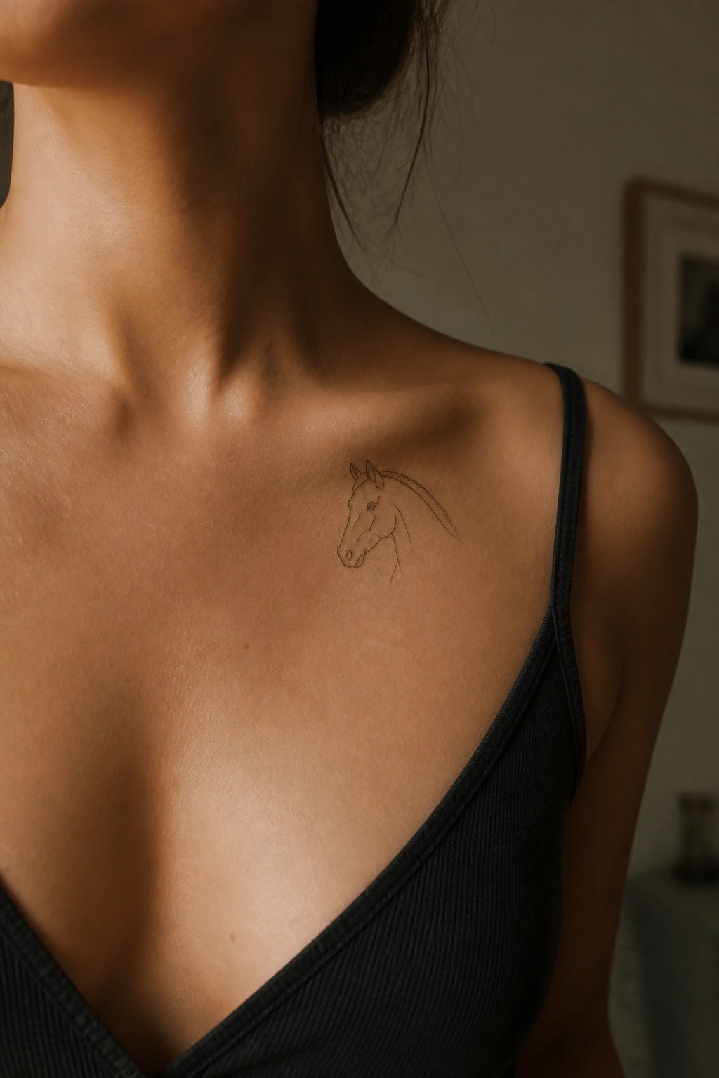 Woman's collarbone with horse head tattoo above black spaghetti strap top