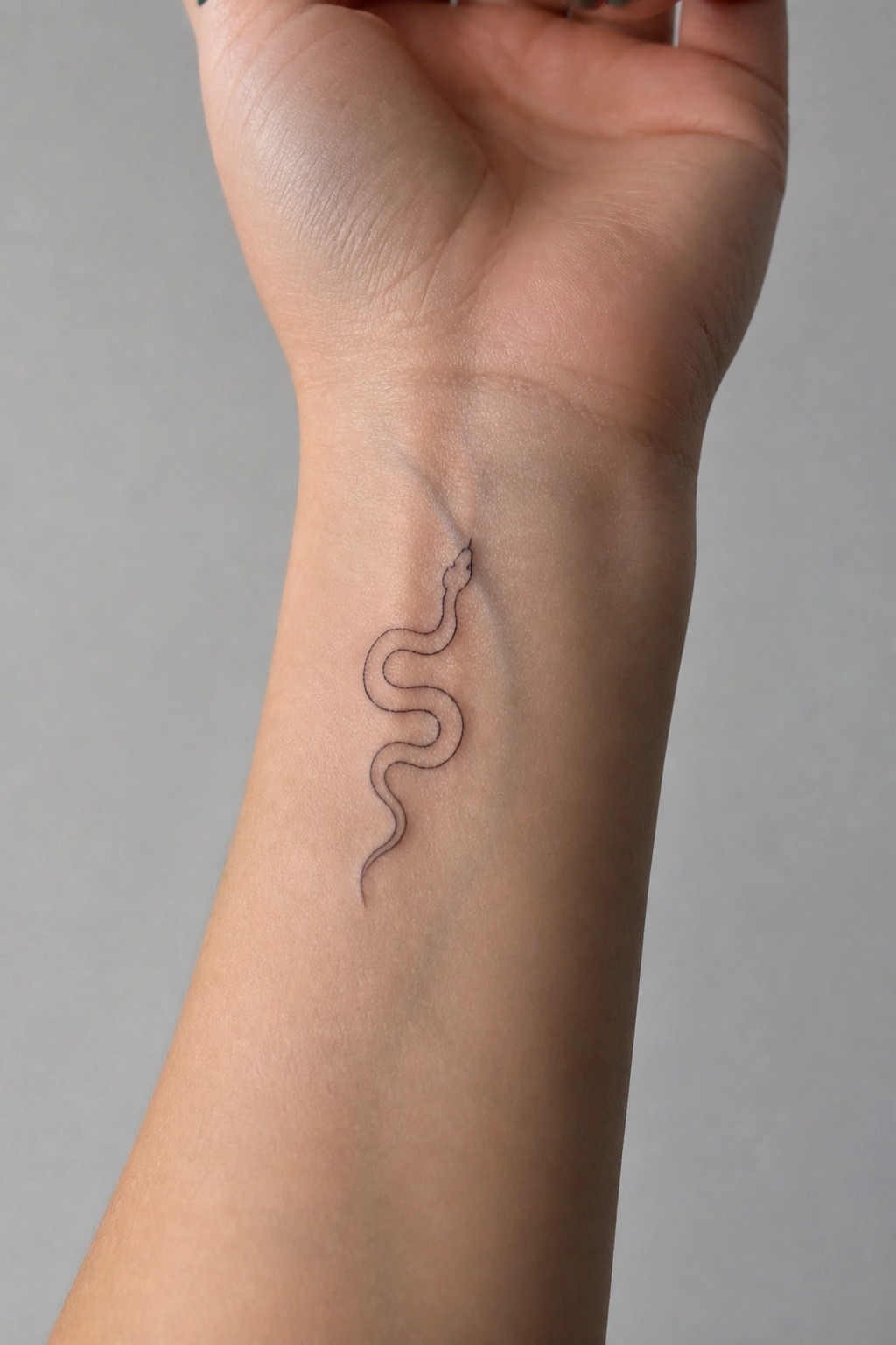 Minimalist black line snake tattoo on the inner wrist