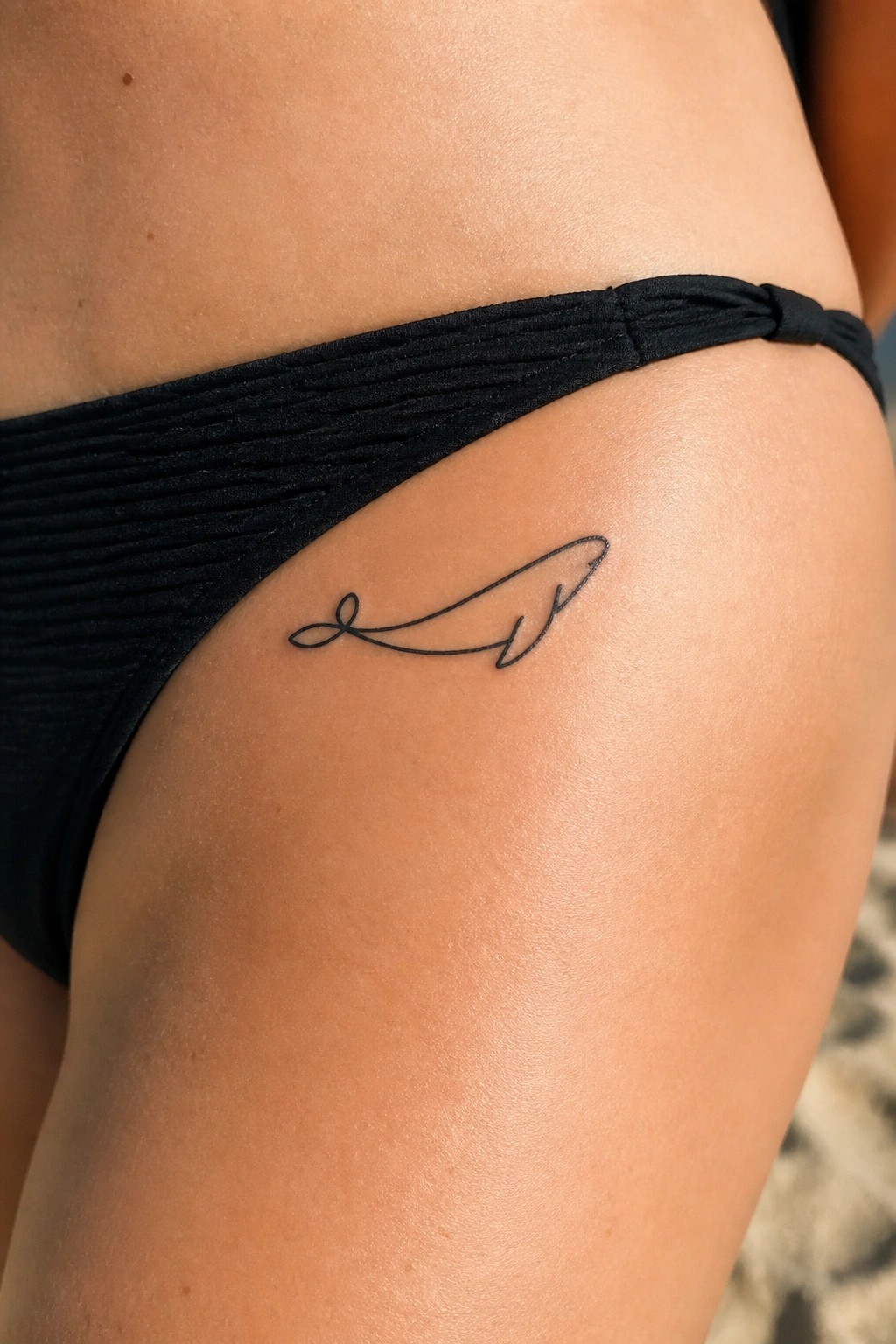Minimalist black whale tattoo on hip above textured black bikini bottoms