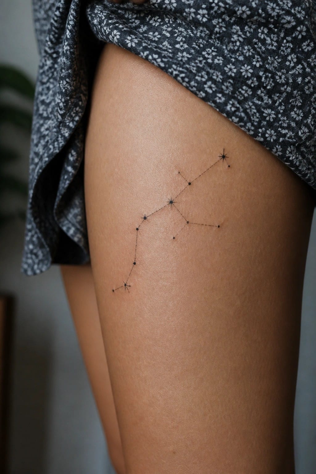 Black constellation tattoo on thigh beneath floral patterned garment