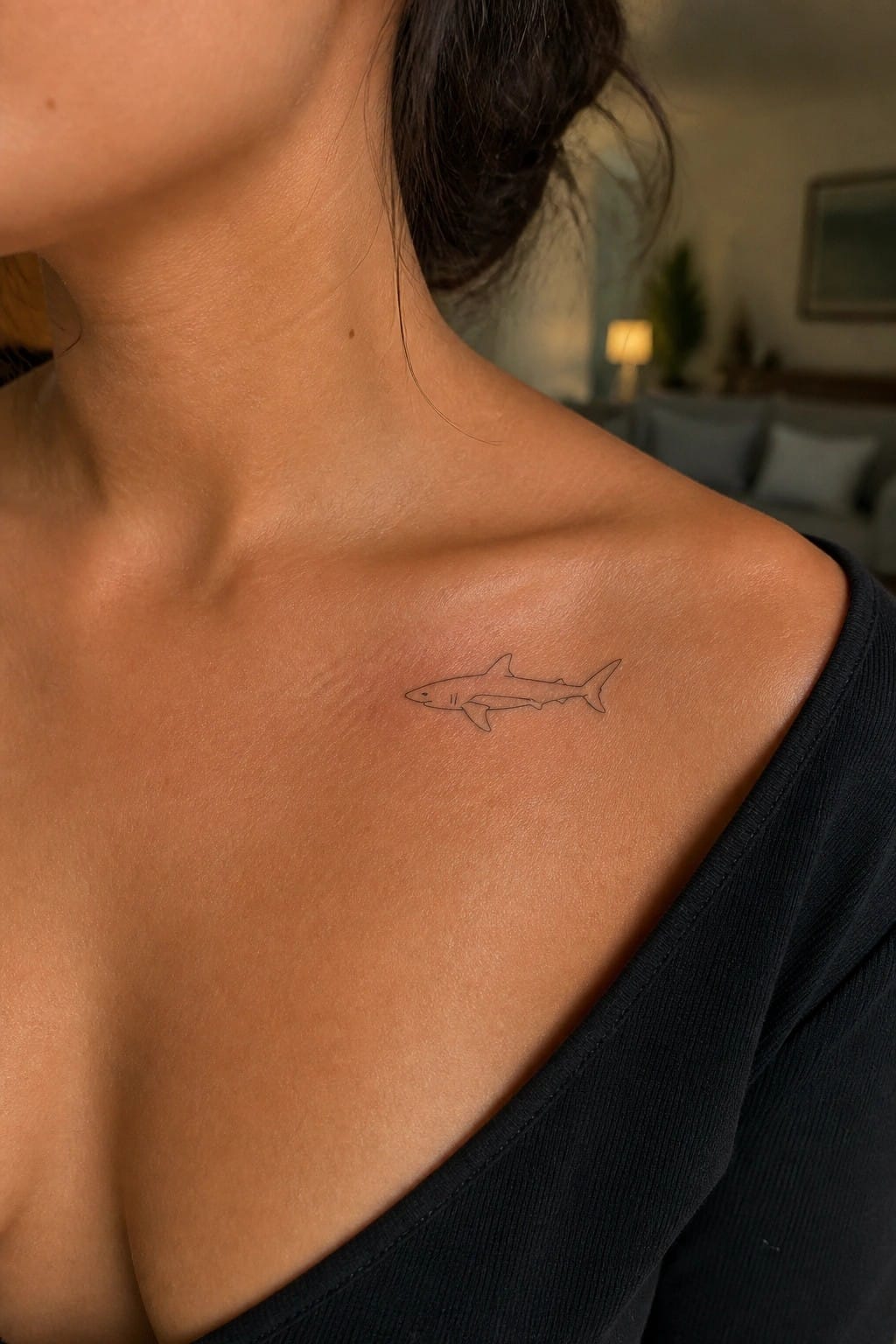 Small shark tattoo on tan shoulder above black off-shoulder top with blurred background