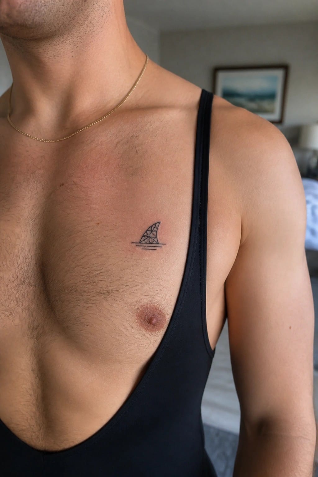 Man's chest with geometric shark fin tattoo in black tank top and gold chain