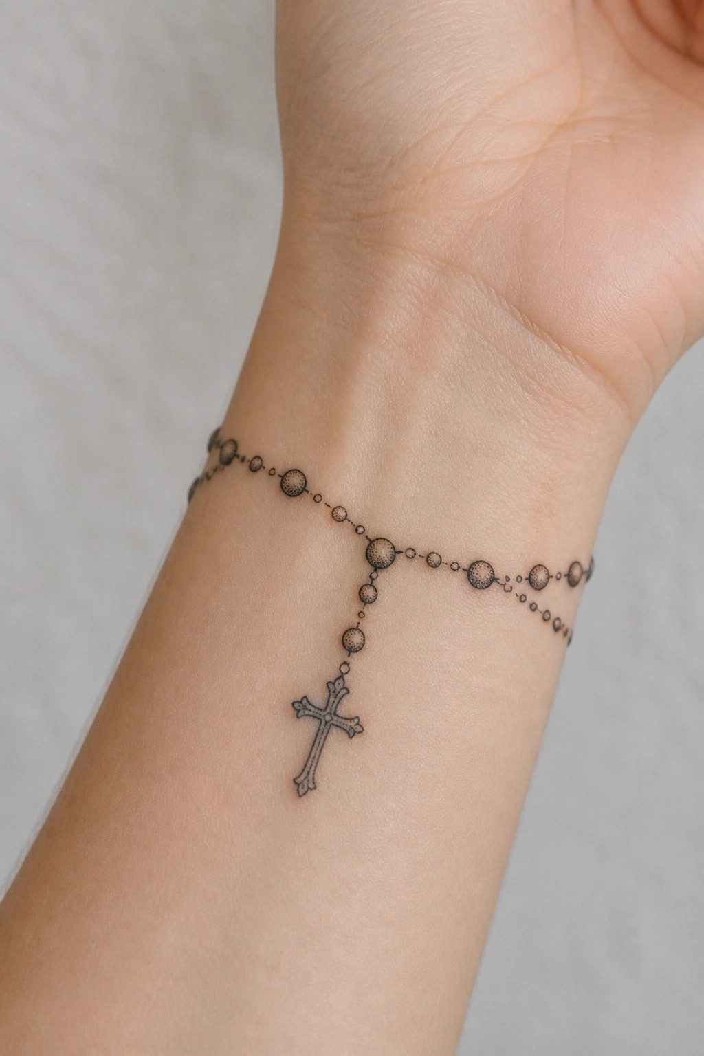 Delicate black rosary tattoo with beads and cross on inner wrist