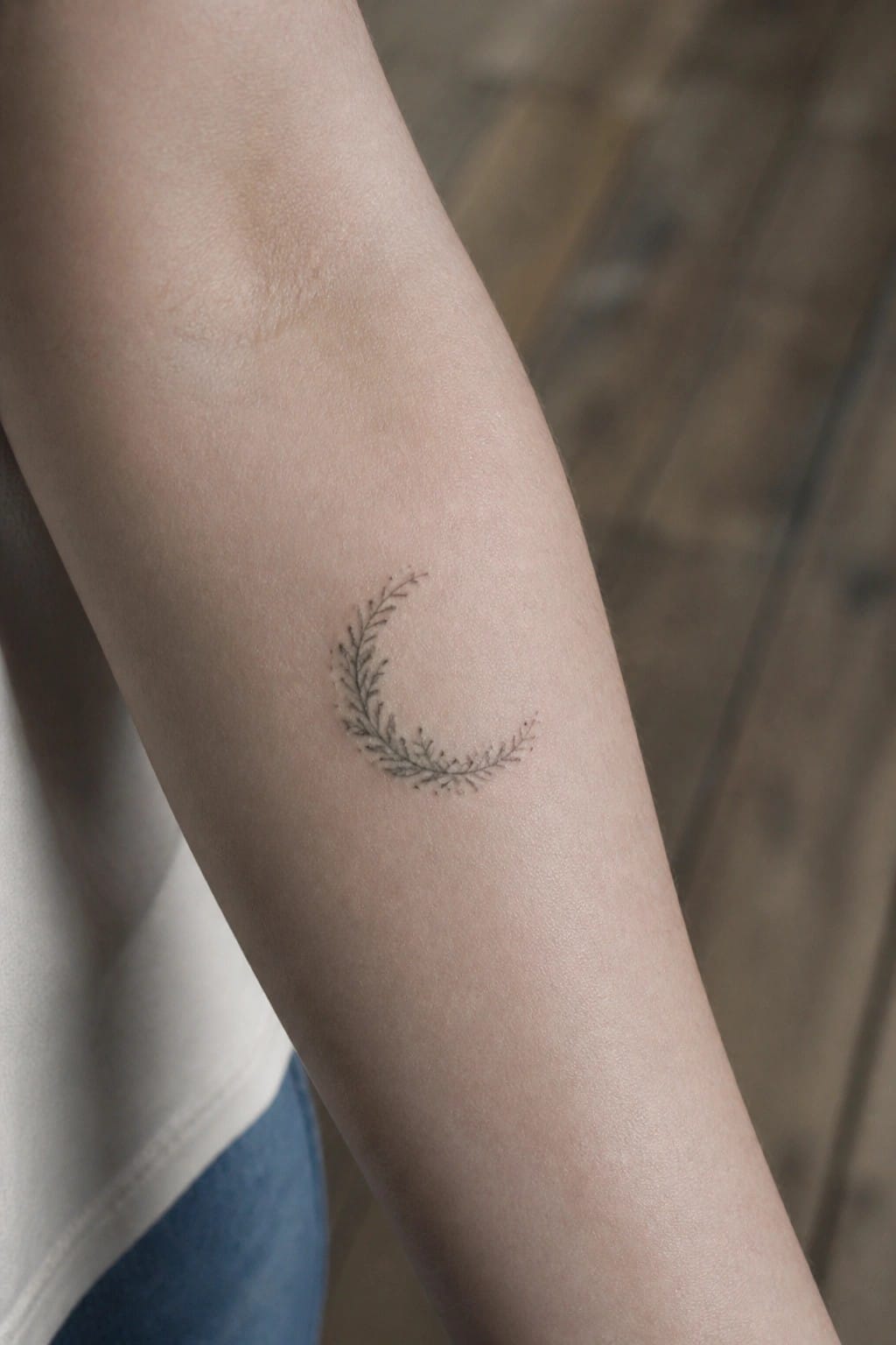 Crescent moon tattoo of delicate leaves on light-skinned forearm with white shirt