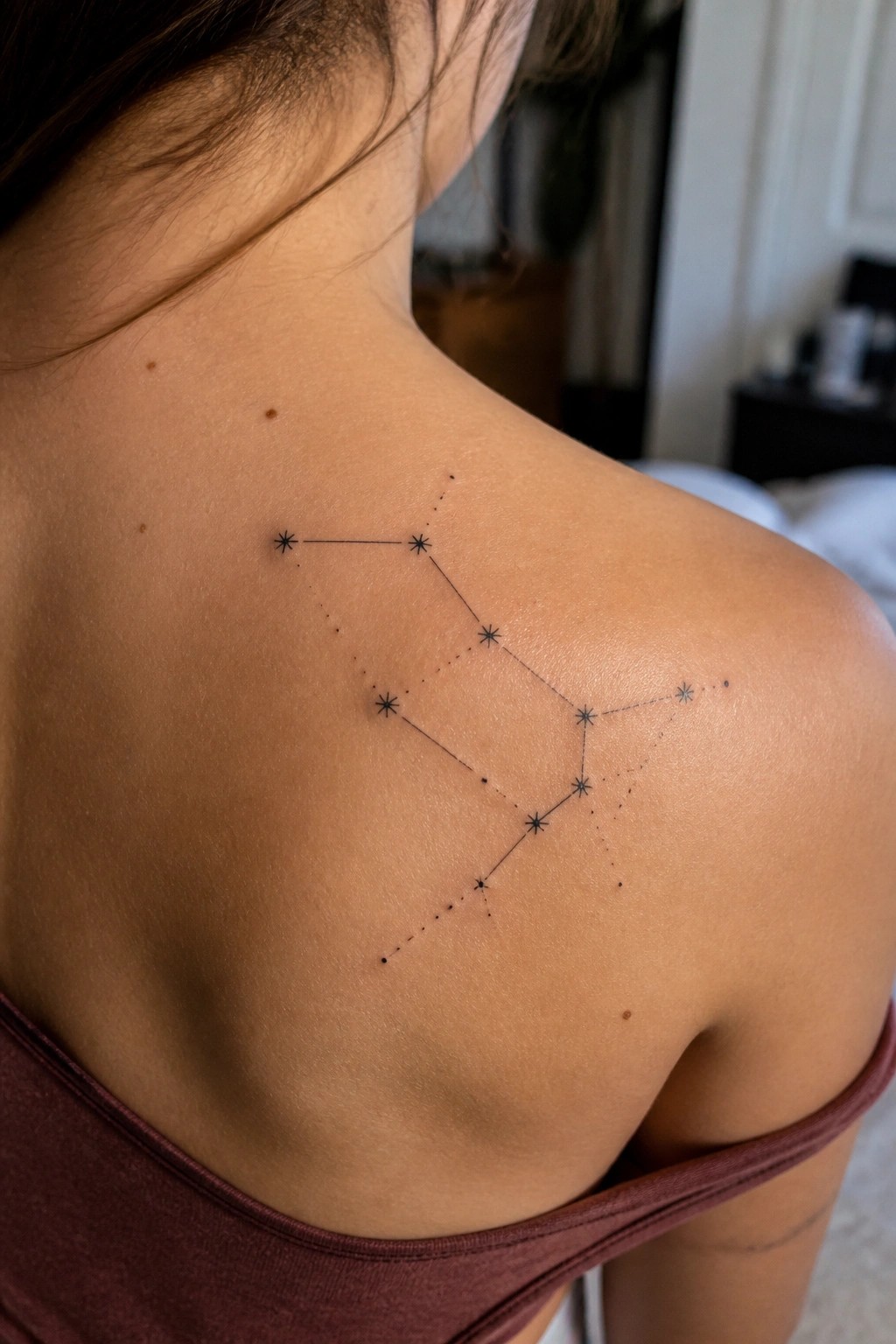 Minimalist constellation tattoo with stars and connecting lines on a woman's upper back and shoulder.