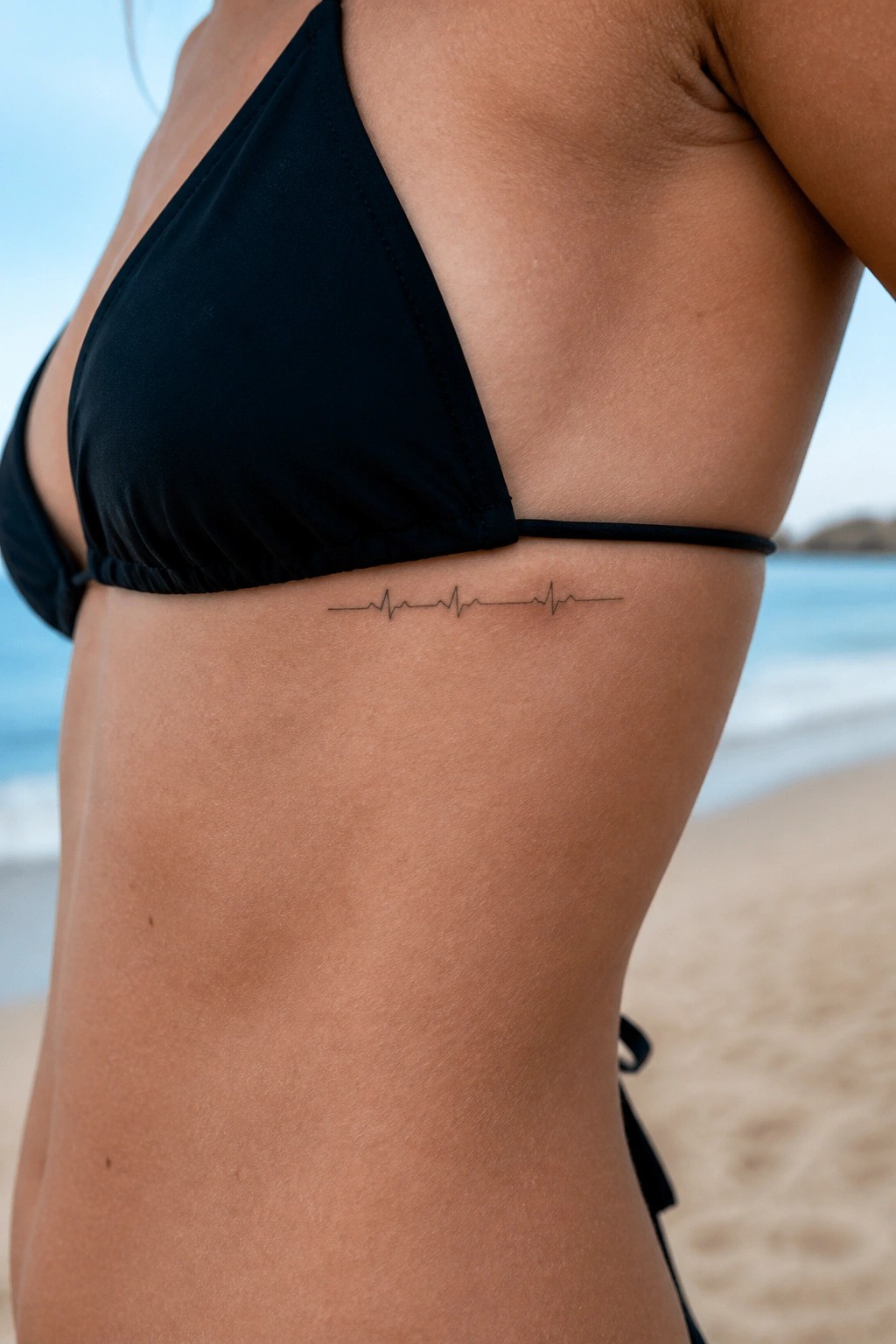 Woman in black bikini with ECG heartbeat tattoo on ribs at sunny beach
