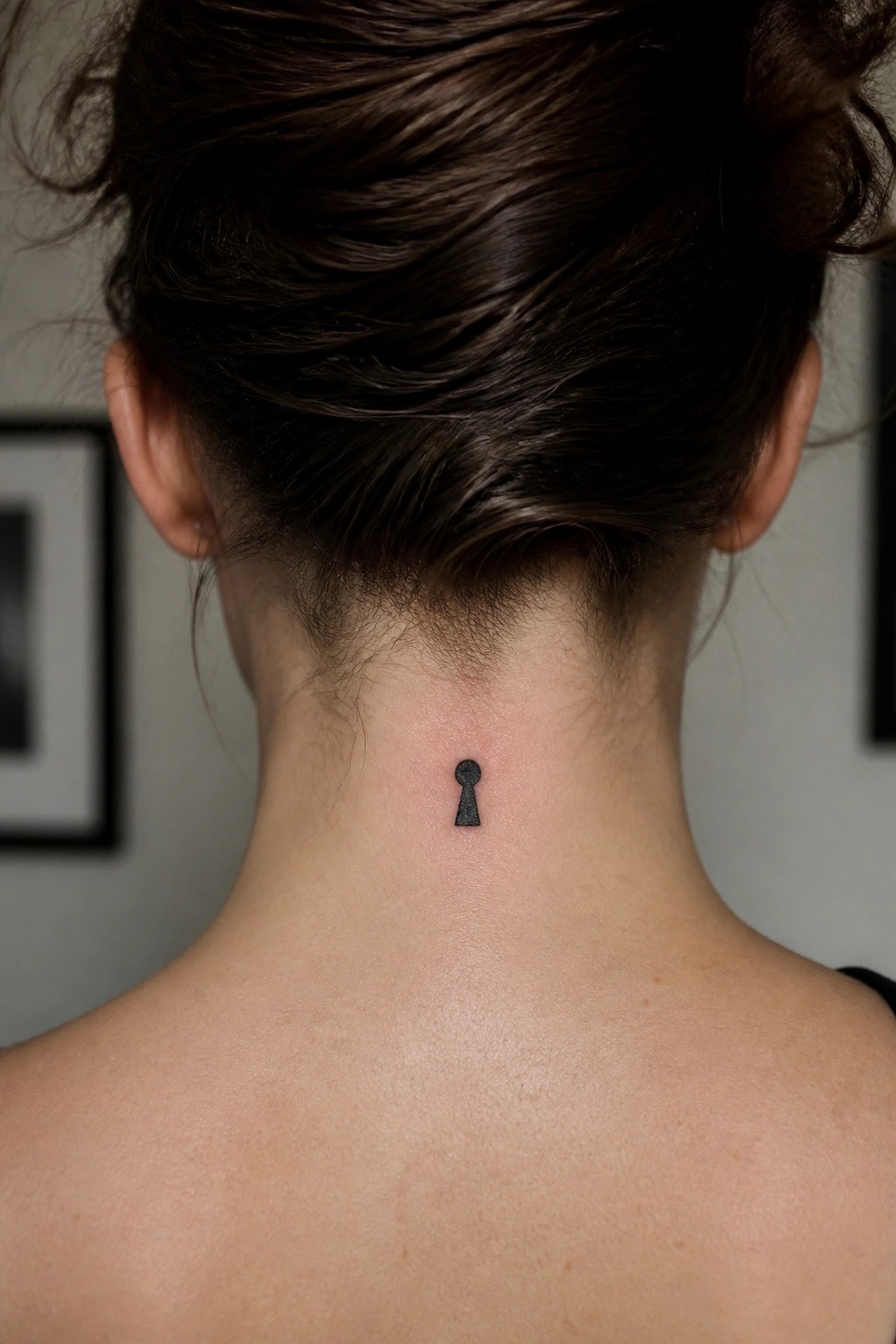 Woman's neck with small black keyhole tattoo below brown hair bun