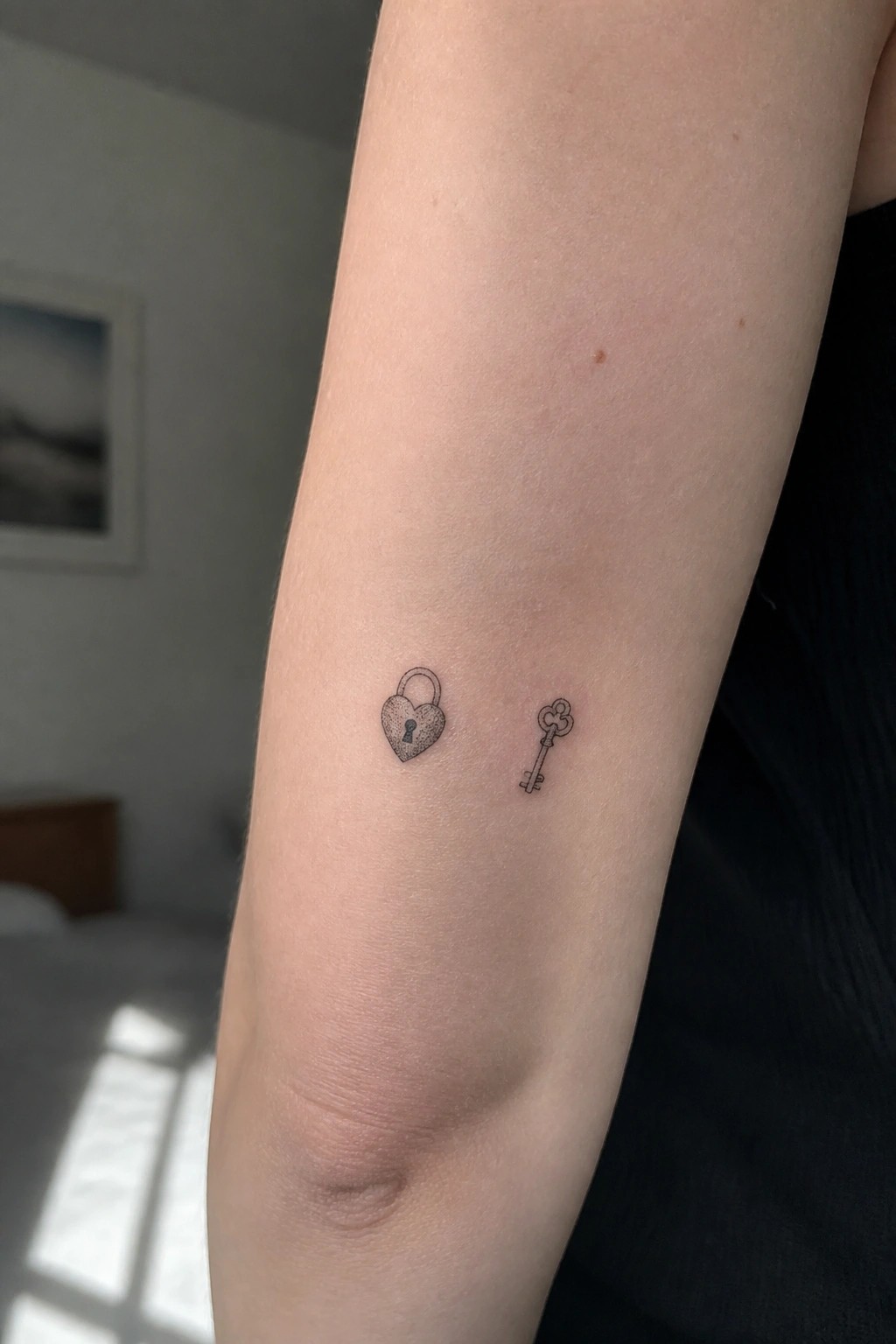 Bare forearm with black heart padlock and key tattoos near elbow.