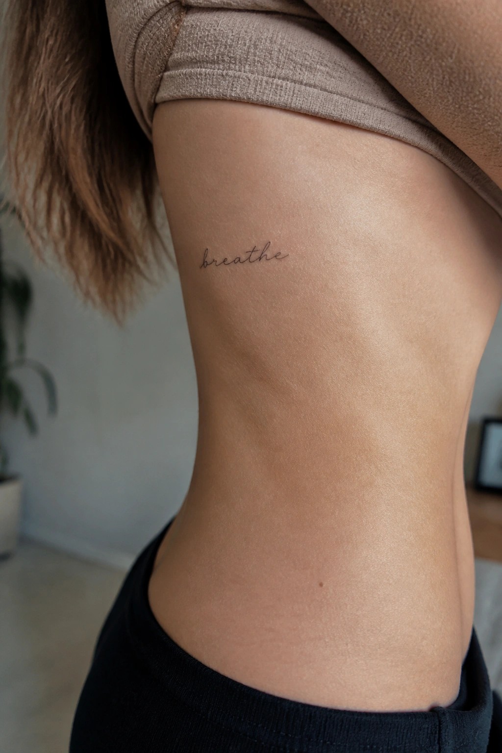Small cursive tattoo of the word breathe on the side of the torso below the ribs