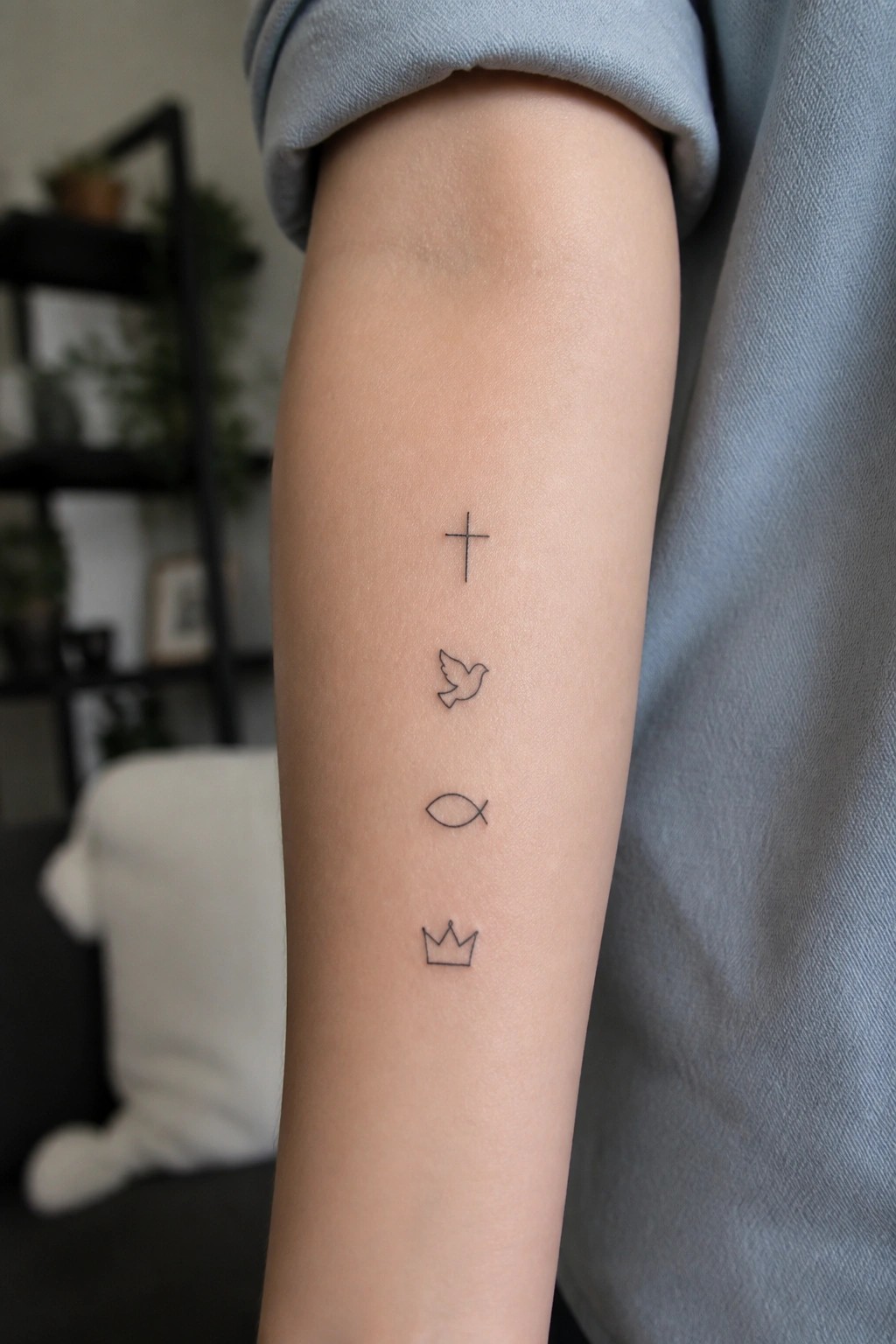 Rolled-up light blue sleeve on arm with vertical cross, dove, fish, and crown tattoos