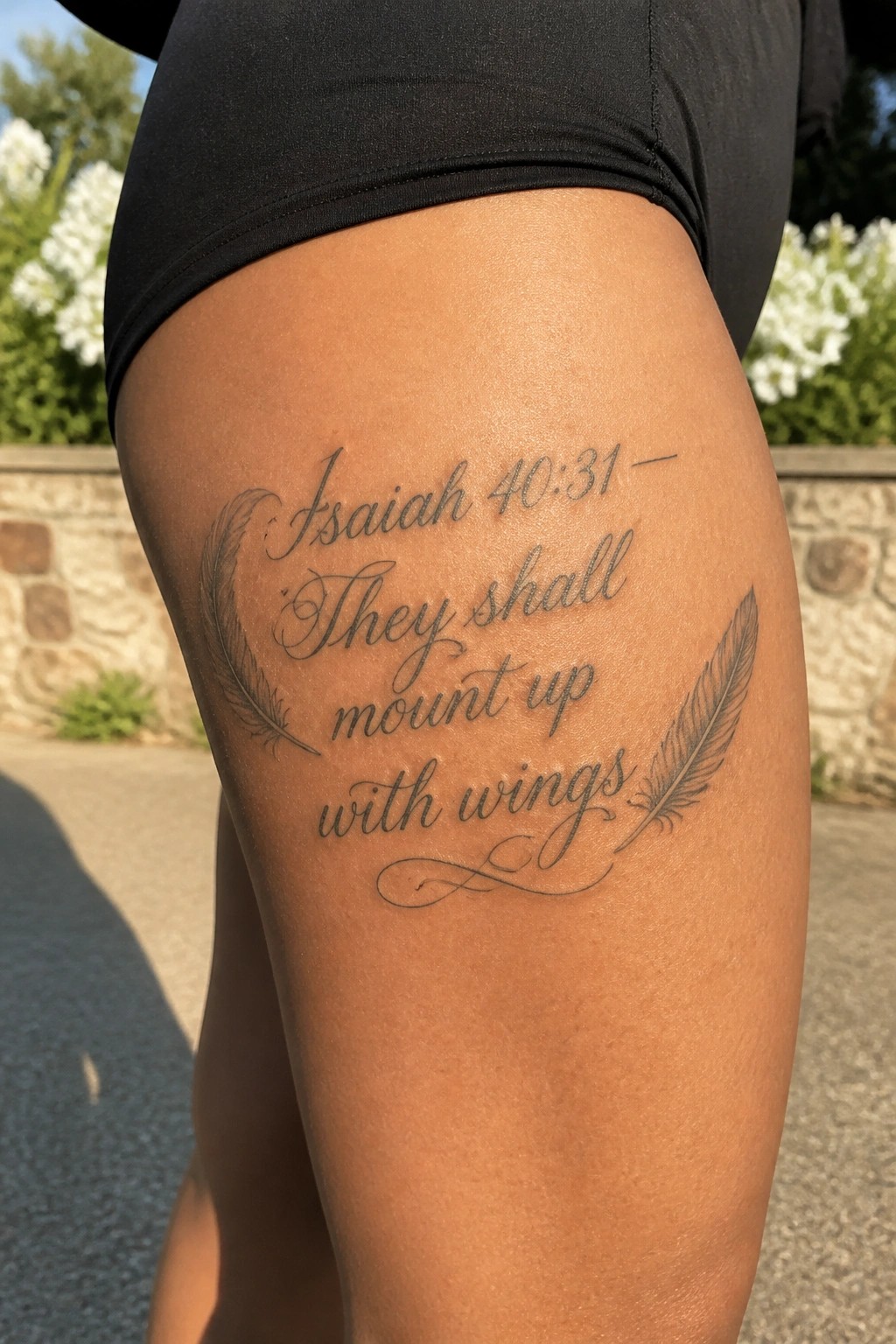Close up of Isaiah 40:31 tattoo on the thigh with script lettering and feather illustrations on both sides.