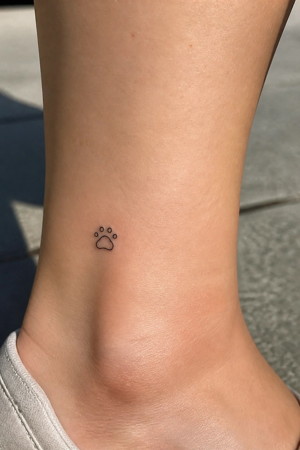 Small black paw print tattoo on light-skinned ankle above white shoe