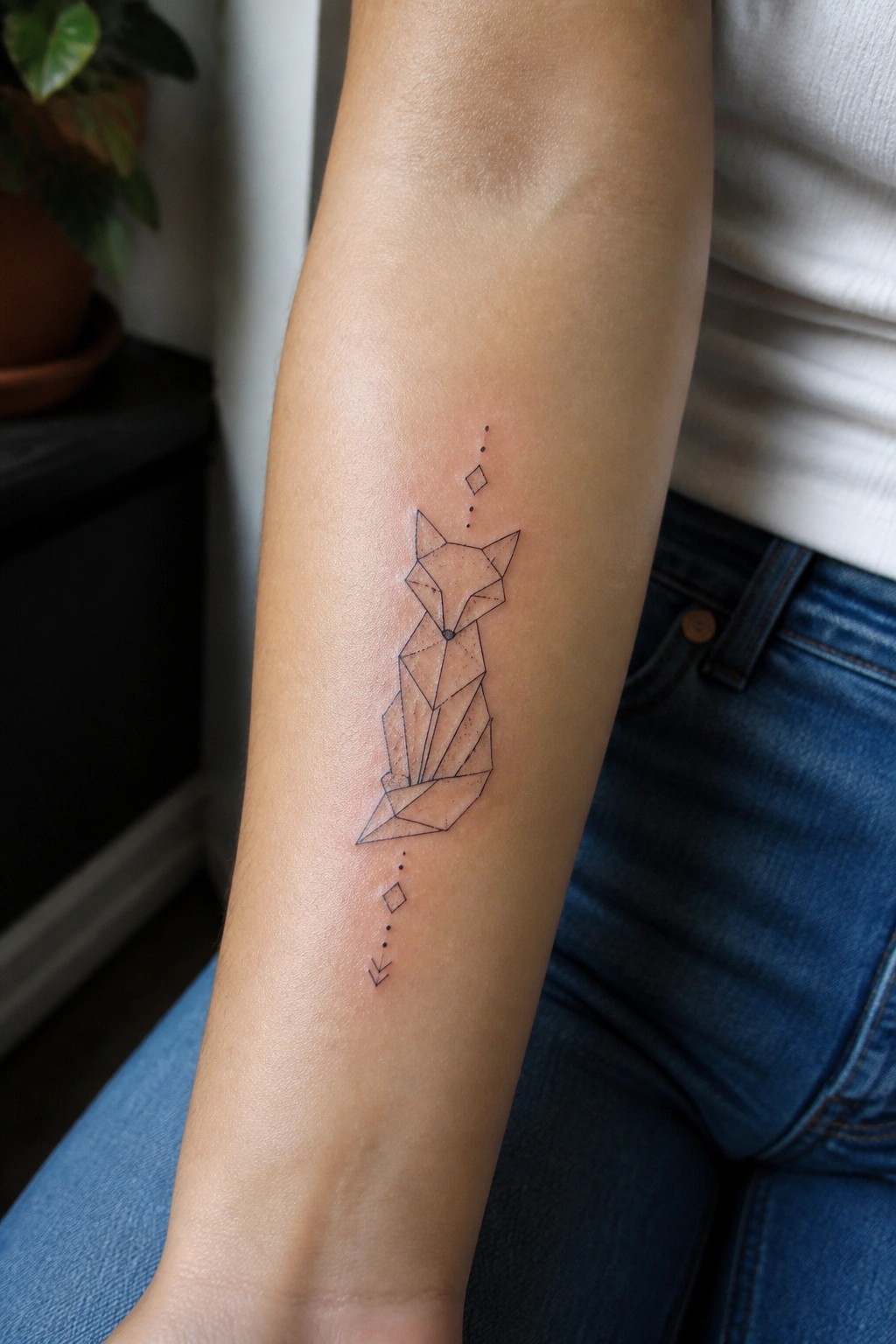 Geometric fox tattoo on forearm with dotted lines, diamonds, and arrows in blue jeans