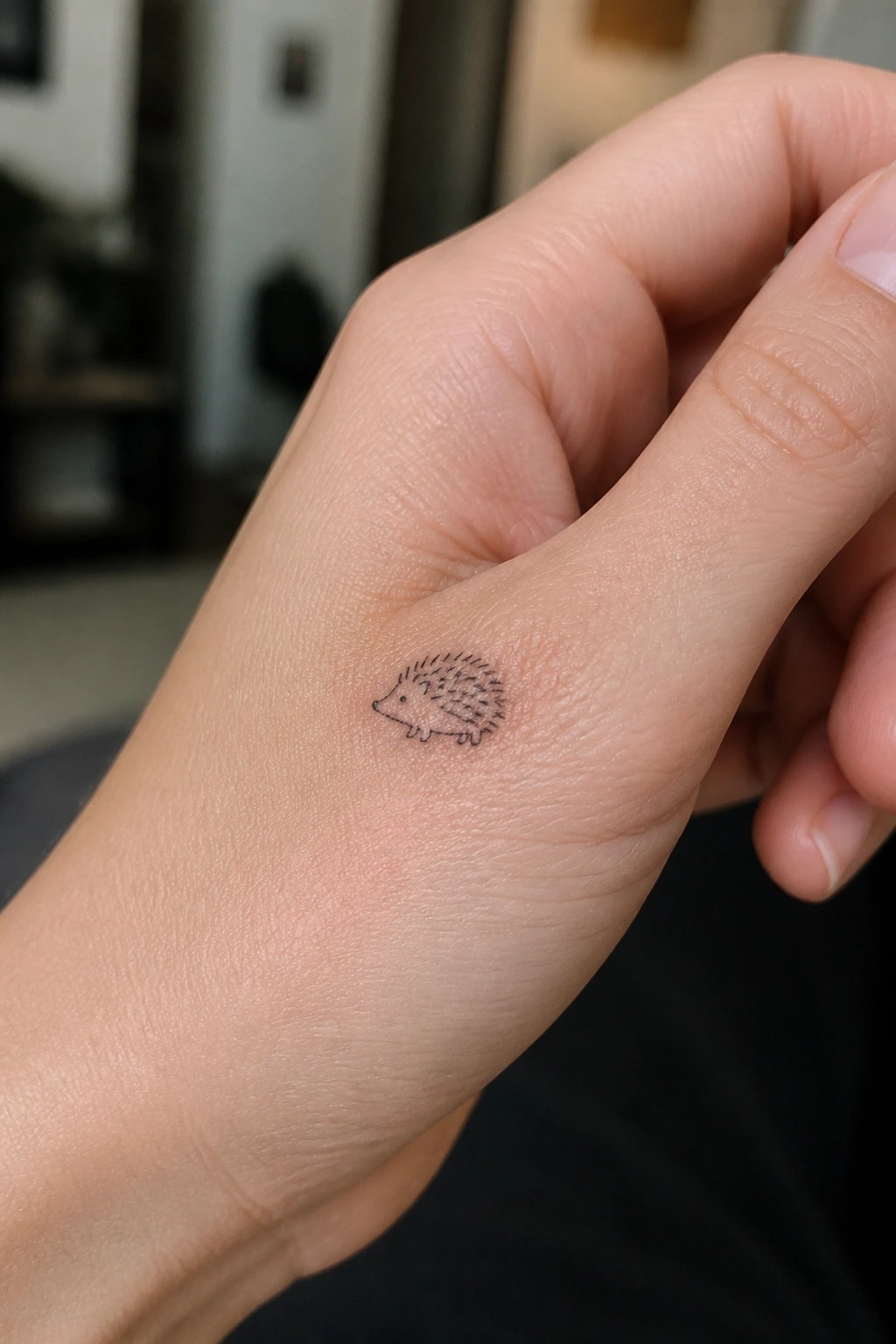 Small black minimalist hedgehog tattoo on the side of a light-skinned hand.