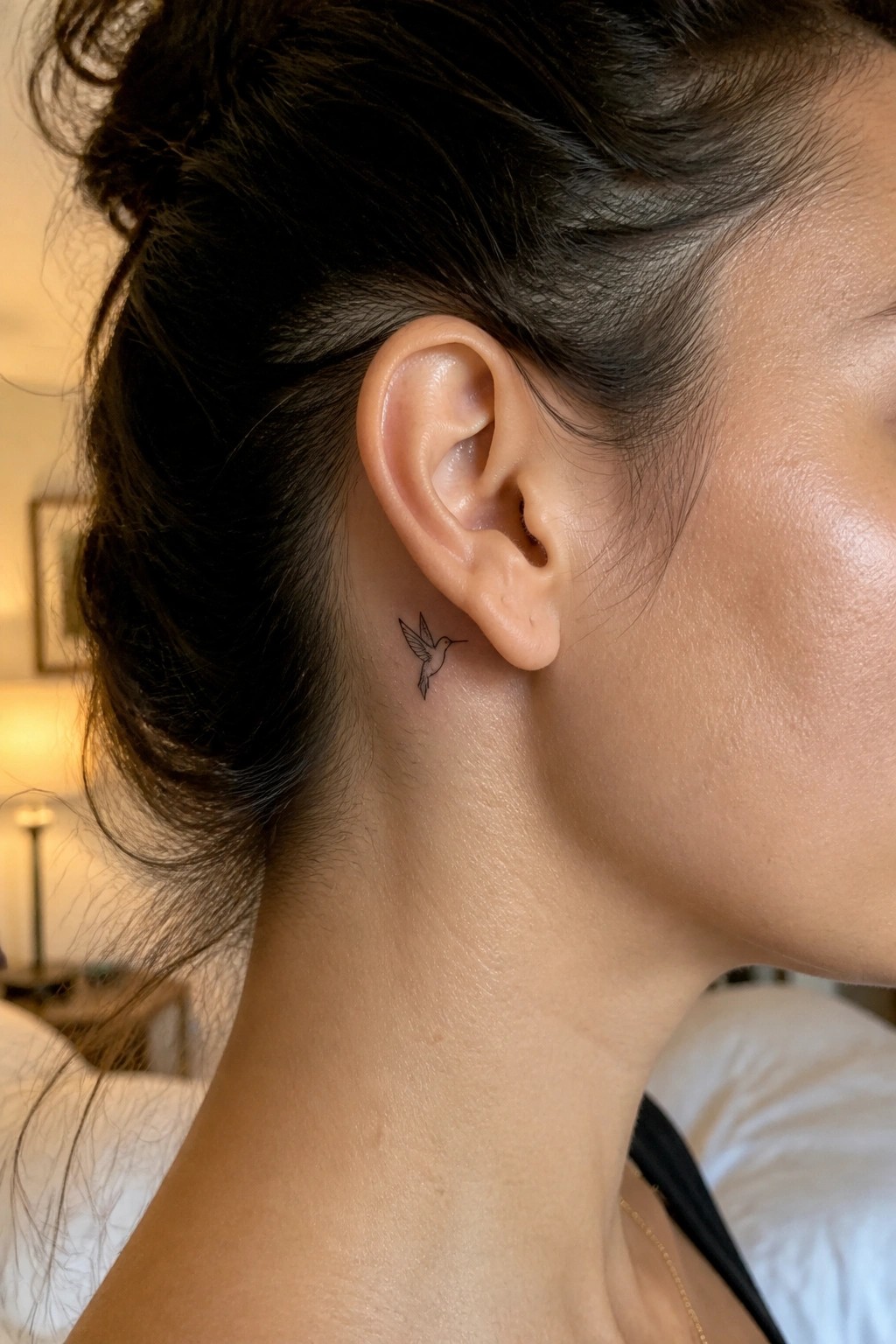Woman with dark bun and small hummingbird tattoo behind her ear