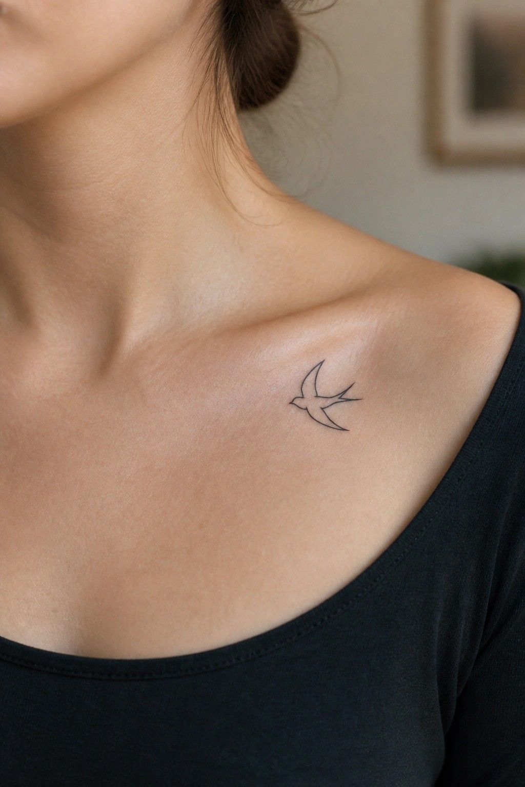 Small bird tattoo on collarbone above black top neckline