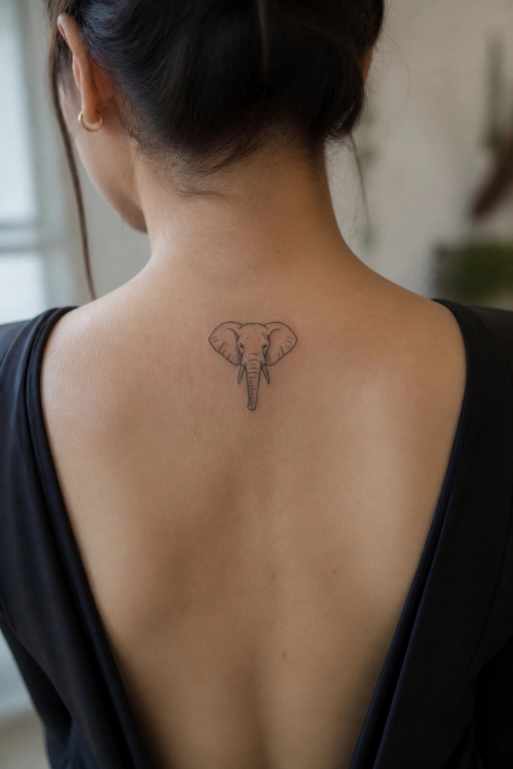 Minimalist black ink elephant head tattoo placed between the shoulder blades on the upper back