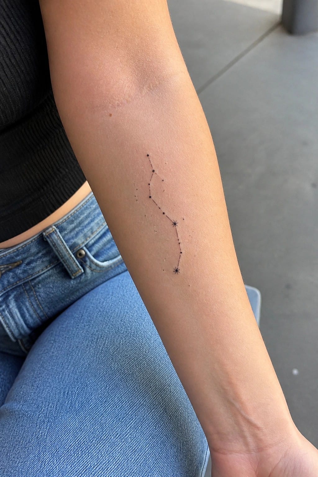 Constellation tattoo of connected dots on forearm above blue jeans and black top