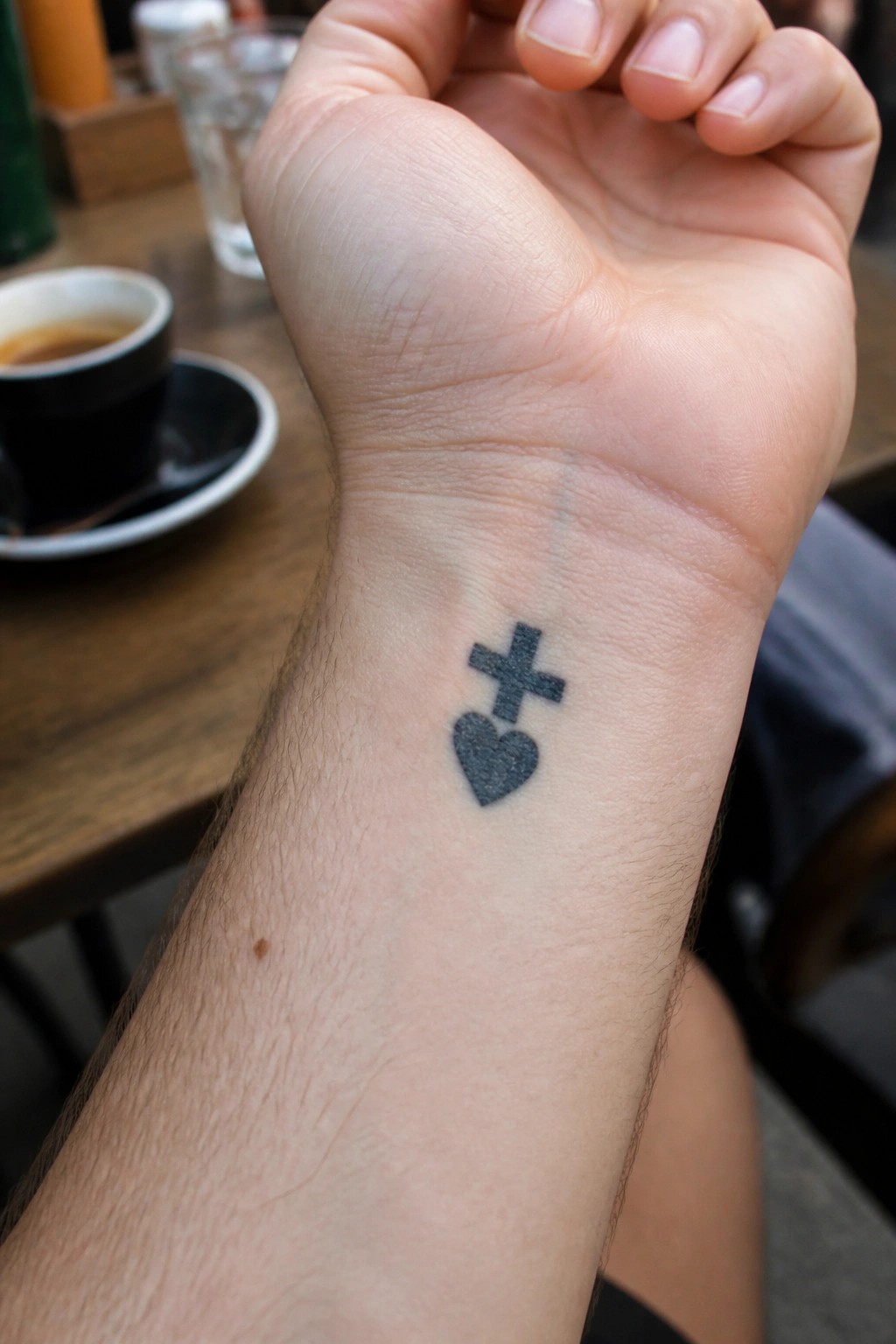 Small black tattoo of a heart with a cross above it on the inner wrist