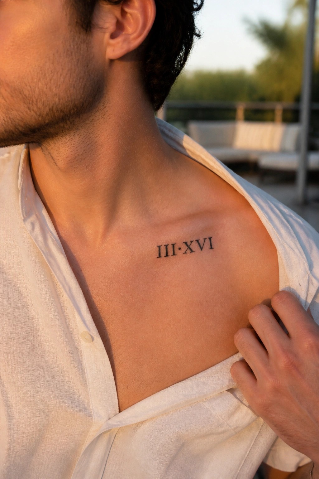 Man's upper chest with III·XVI tattoo, open white shirt, hand resting on shoulder in sunlight