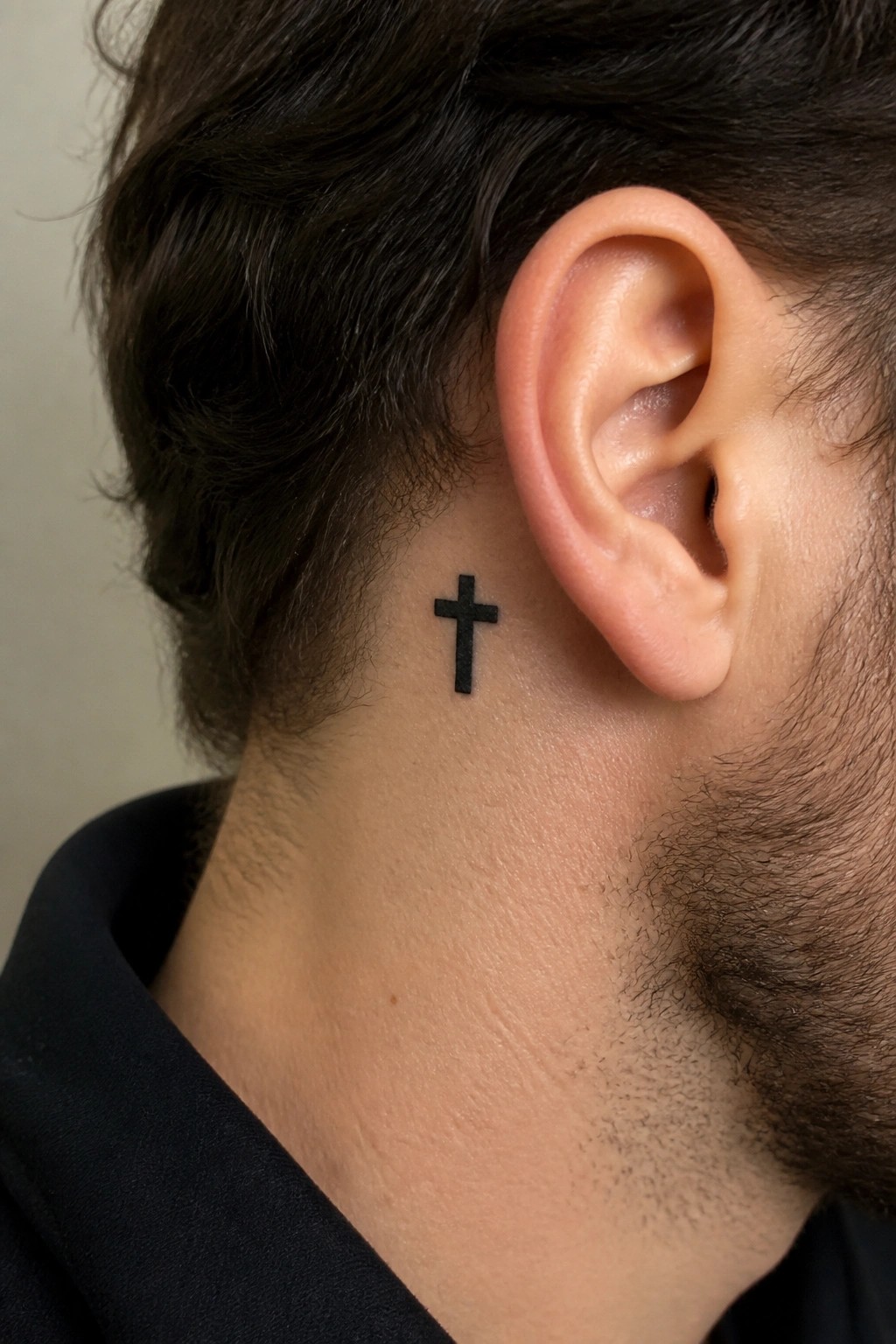 Man's neck with small black cross tattoo behind ear and dark hair