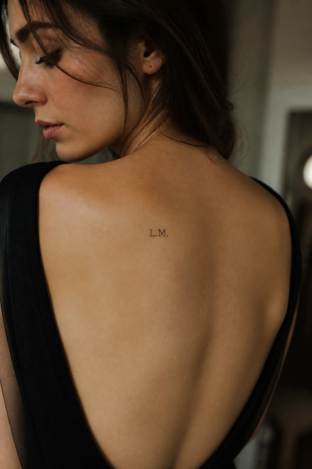 Woman's back with L.M. tattoo in black backless dress, dark hair flowing.