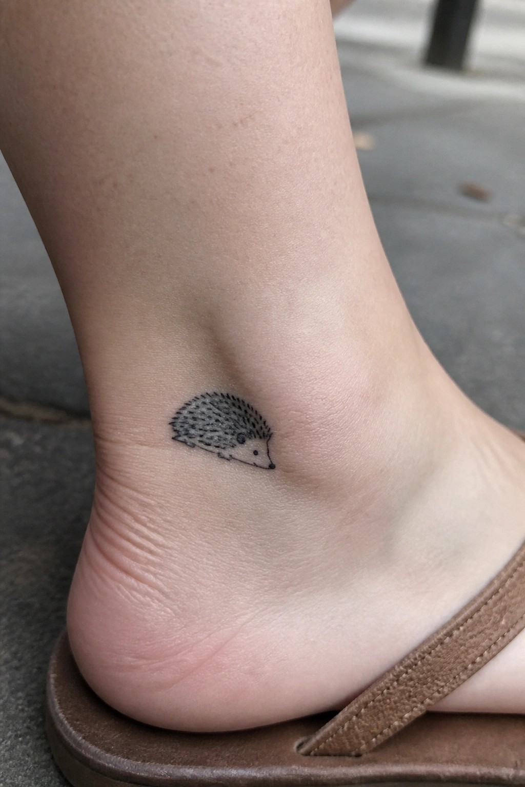 Small black ink hedgehog tattoo on the ankle above the foot