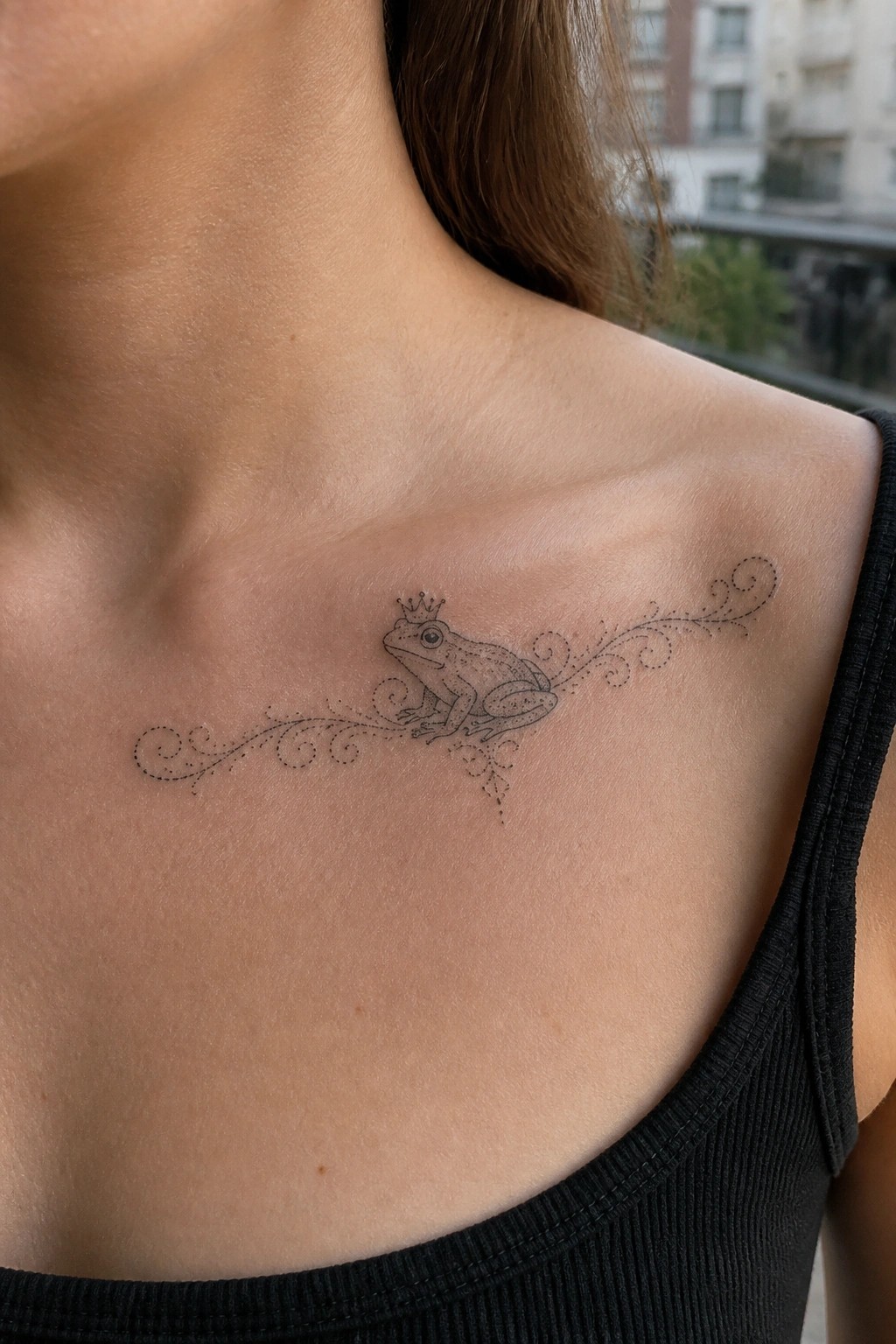 Crowned frog tattoo with swirling vines on shoulder above black tank top.