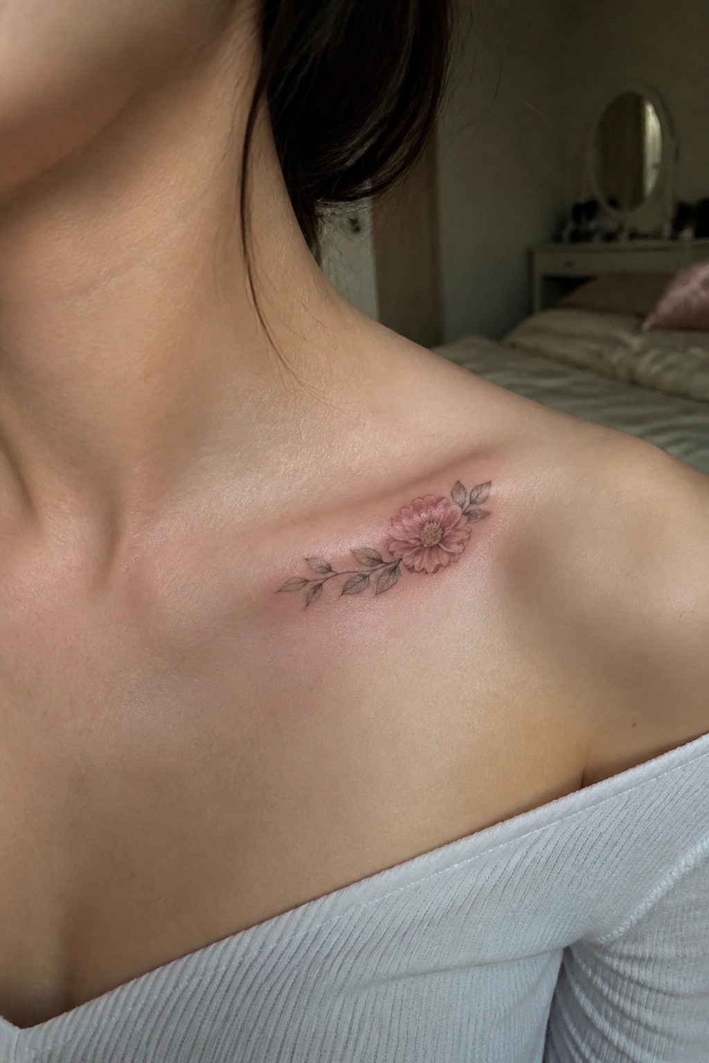Pink flower tattoo with leaves on shoulder over white off-shoulder top